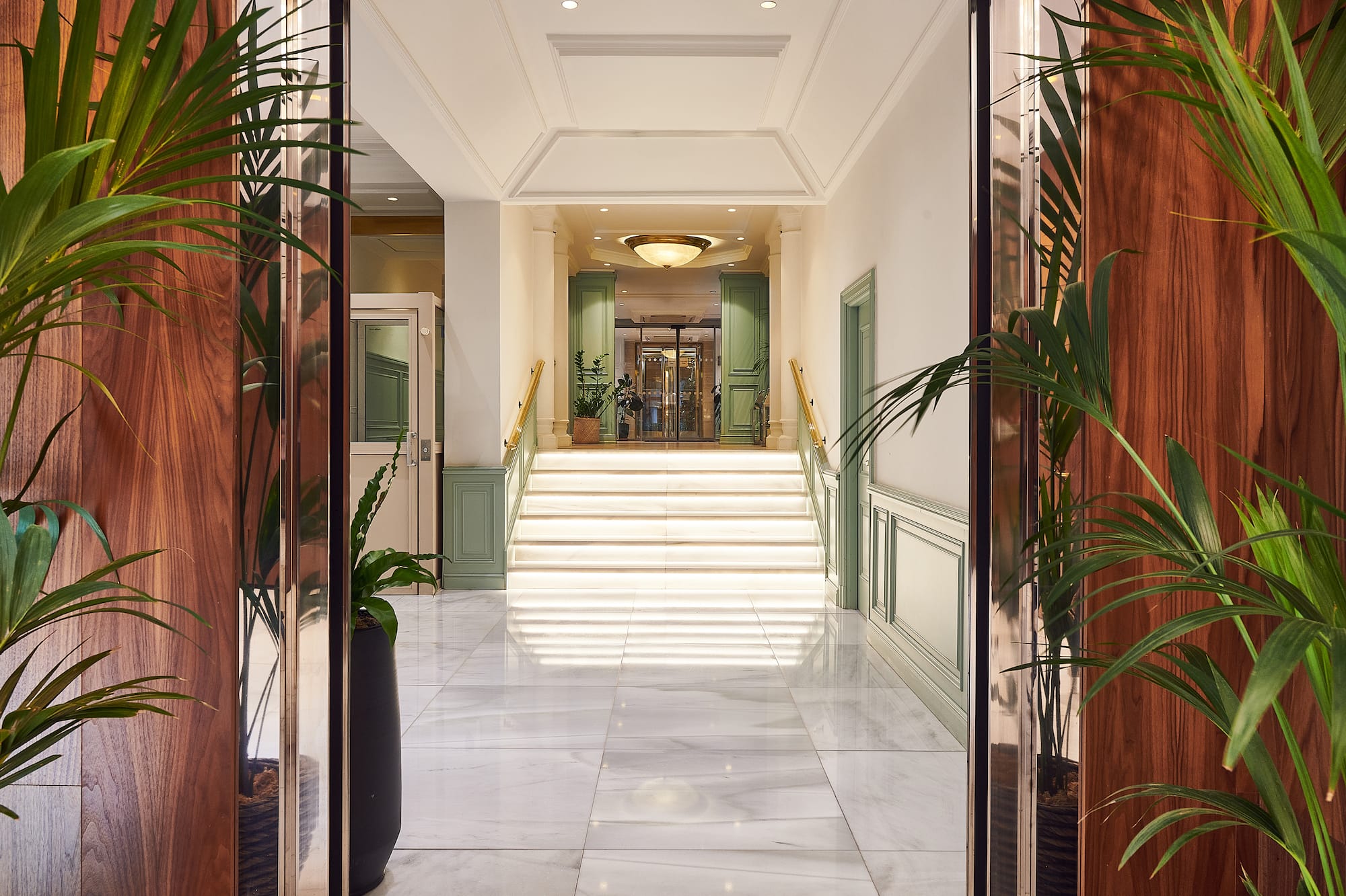 Luxury hotel lobby, grand marble staircase, wood paneling, elegant plants.