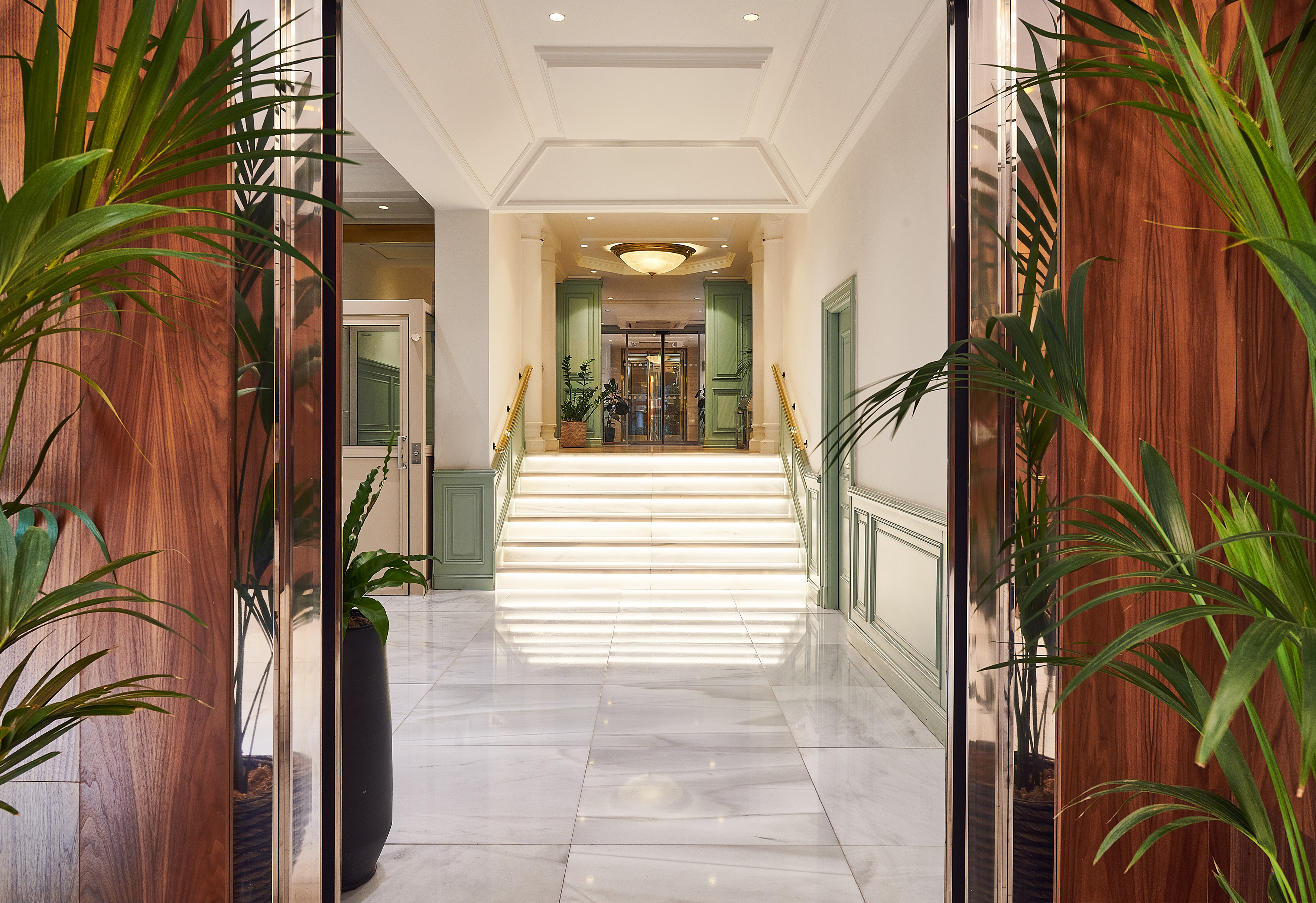Luxury hotel lobby, grand marble staircase, wood paneling, elegant plants.