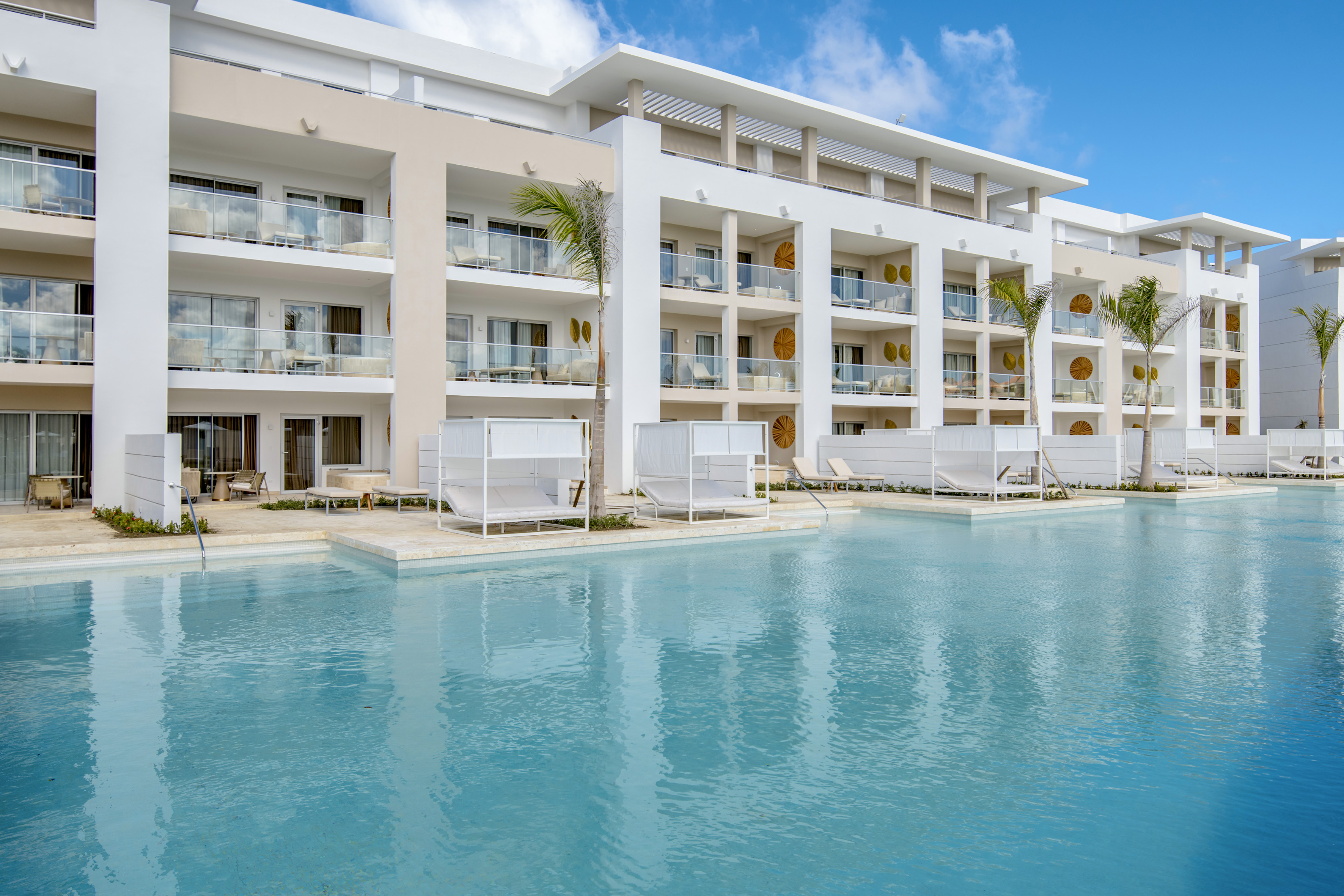 Luxury resort with large blue swimming pool, white cabanas, and modern balconies.