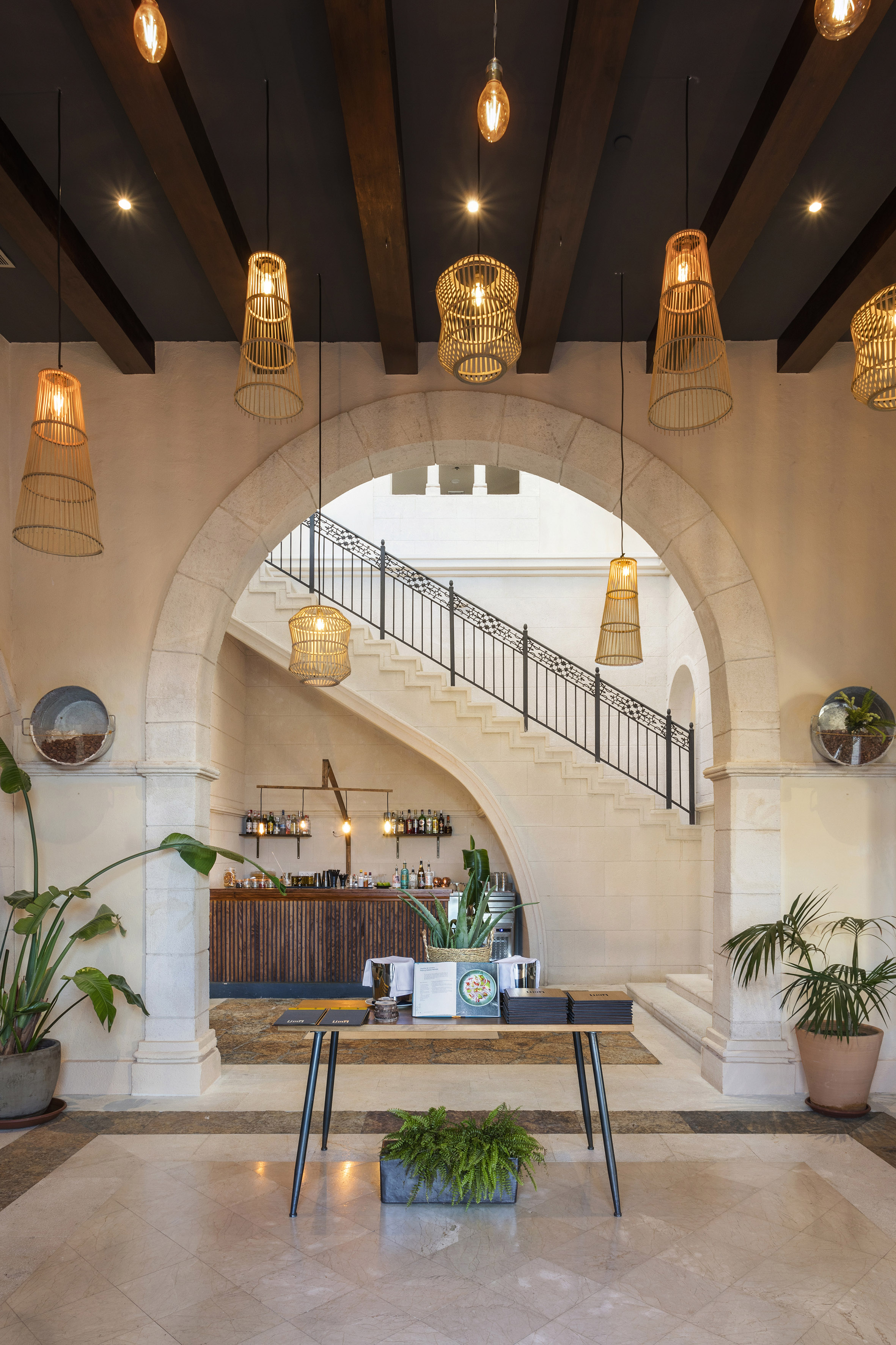 Hotel lobby with arched stone entrance, grand staircase, and rattan pendant lights.