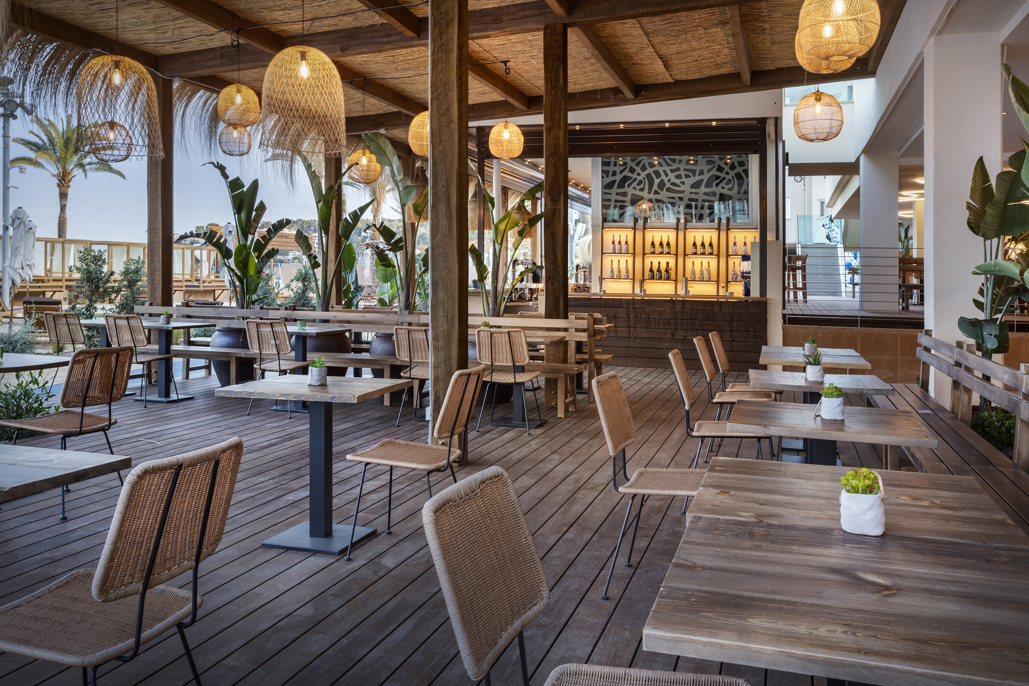 Tropical outdoor restaurant patio with woven chairs, wooden tables, and bar.