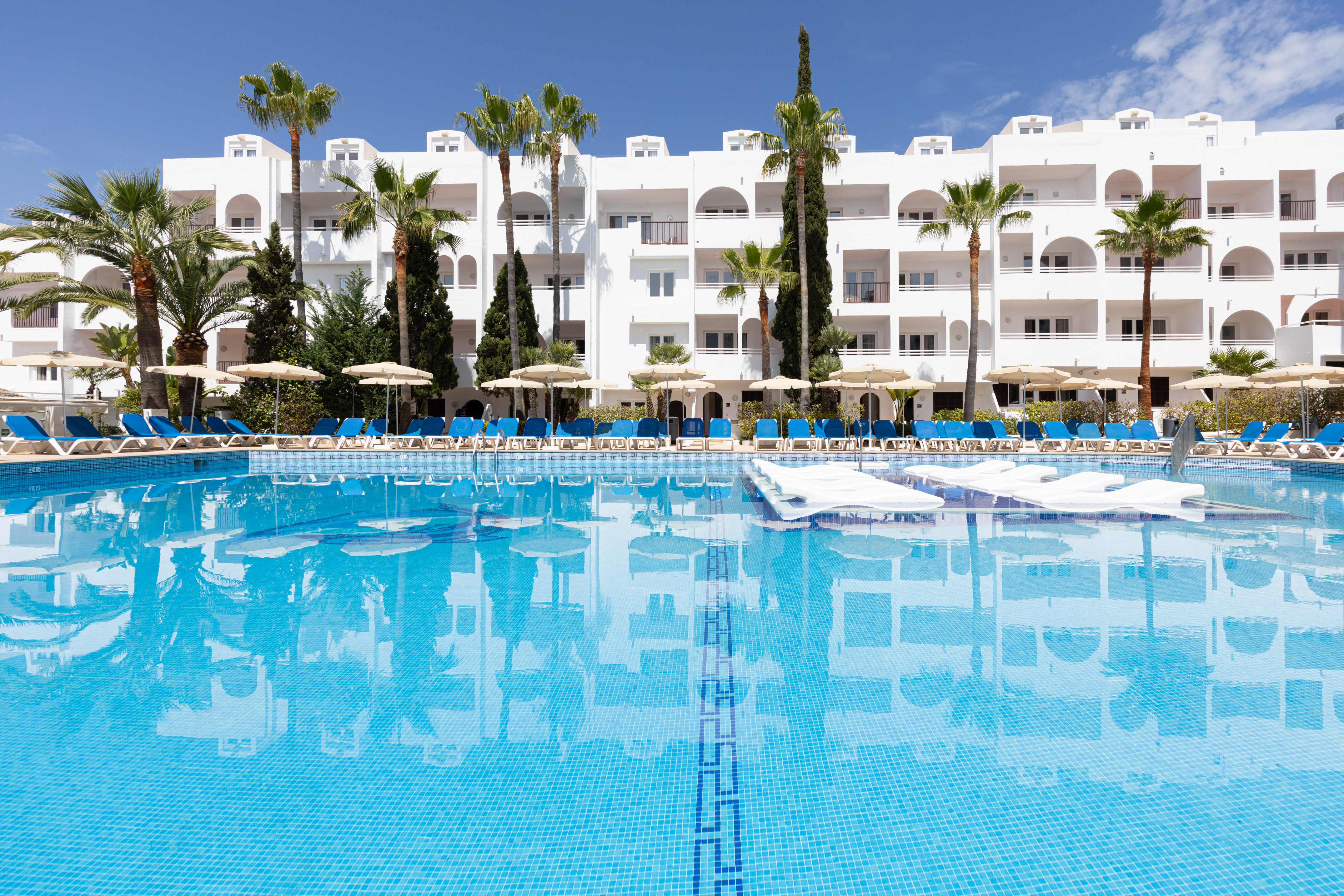 Tropical hotel resort pool, palm trees, and white building.