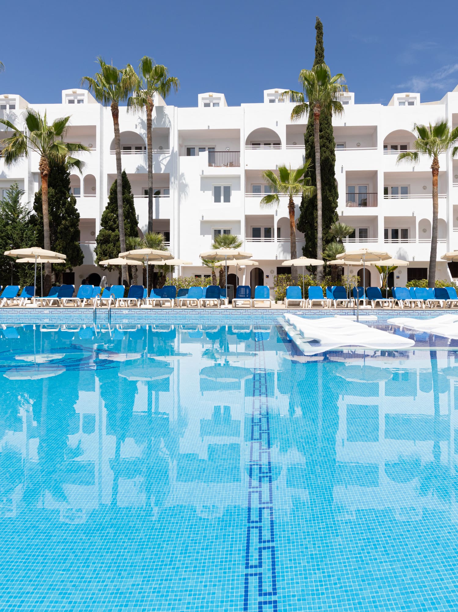 Tropical hotel resort pool, palm trees, and white building.