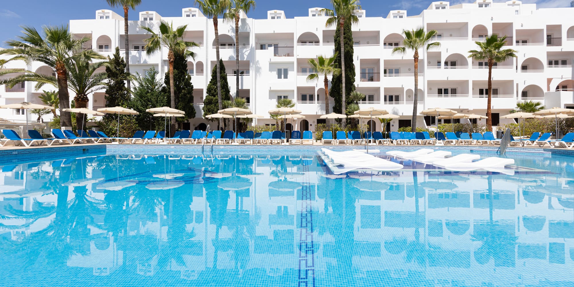 Tropical hotel resort pool, palm trees, and white building.