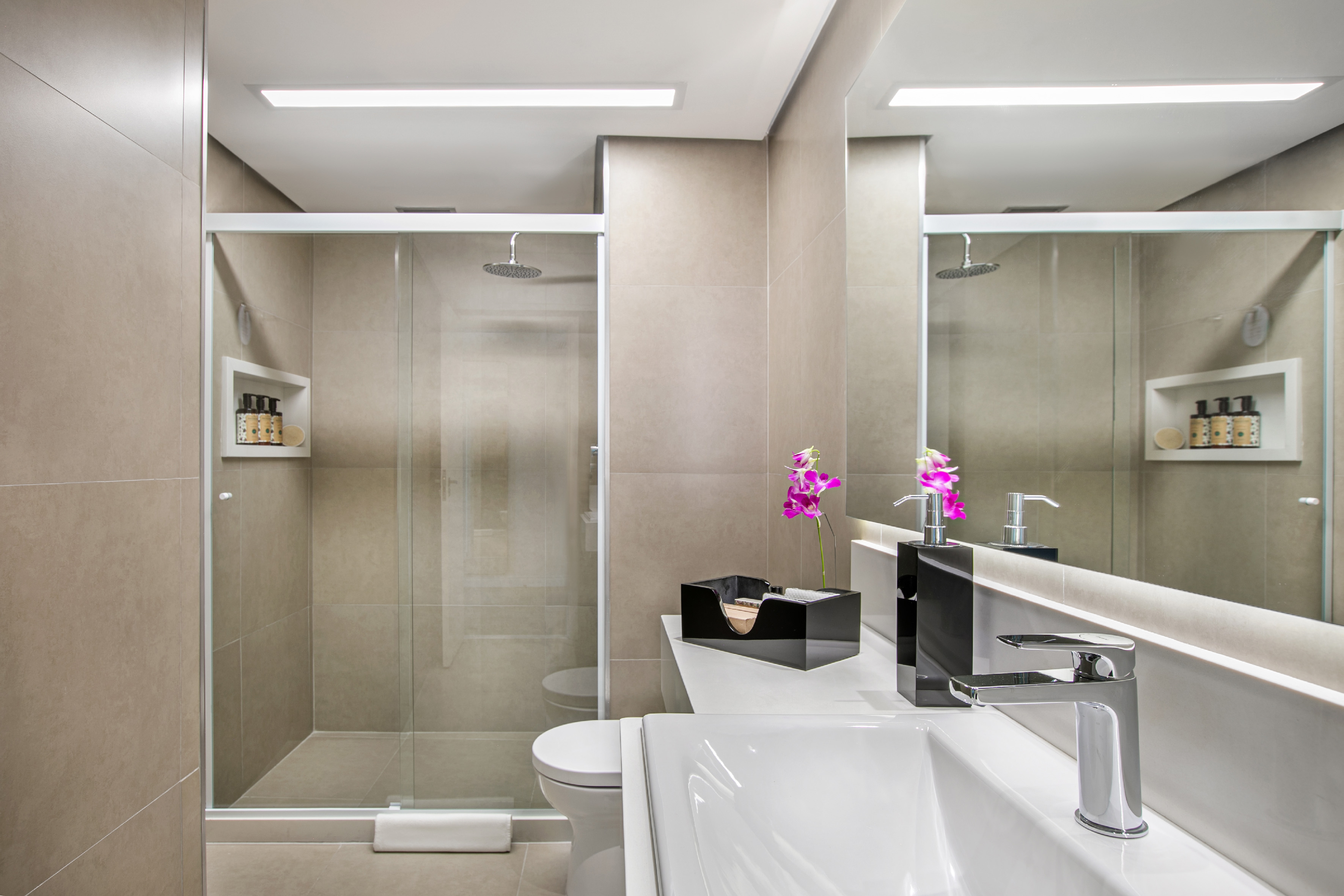 Modern beige bathroom with glass shower, vanity sink, and toilet.