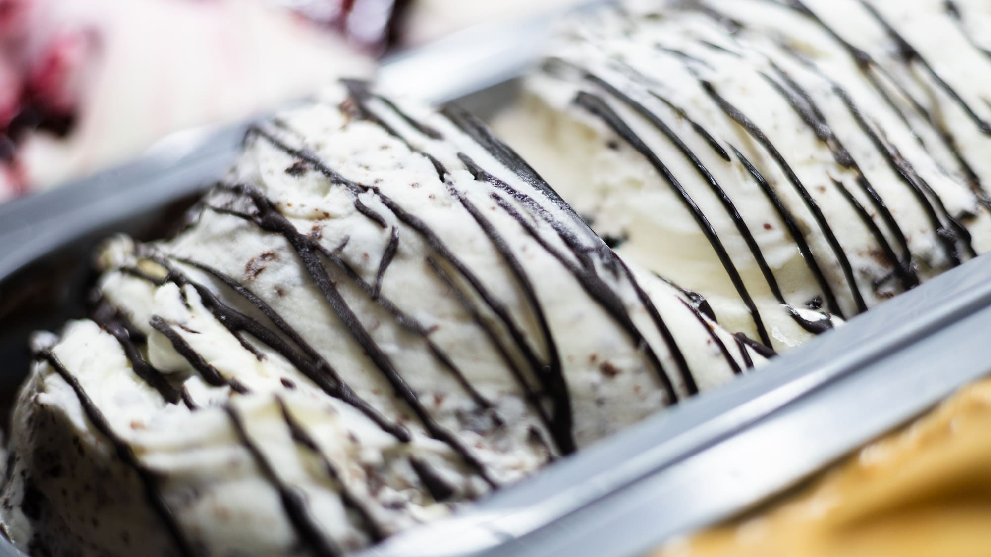 Creamy cookies and cream ice cream with chocolate stripes in a metal pan.