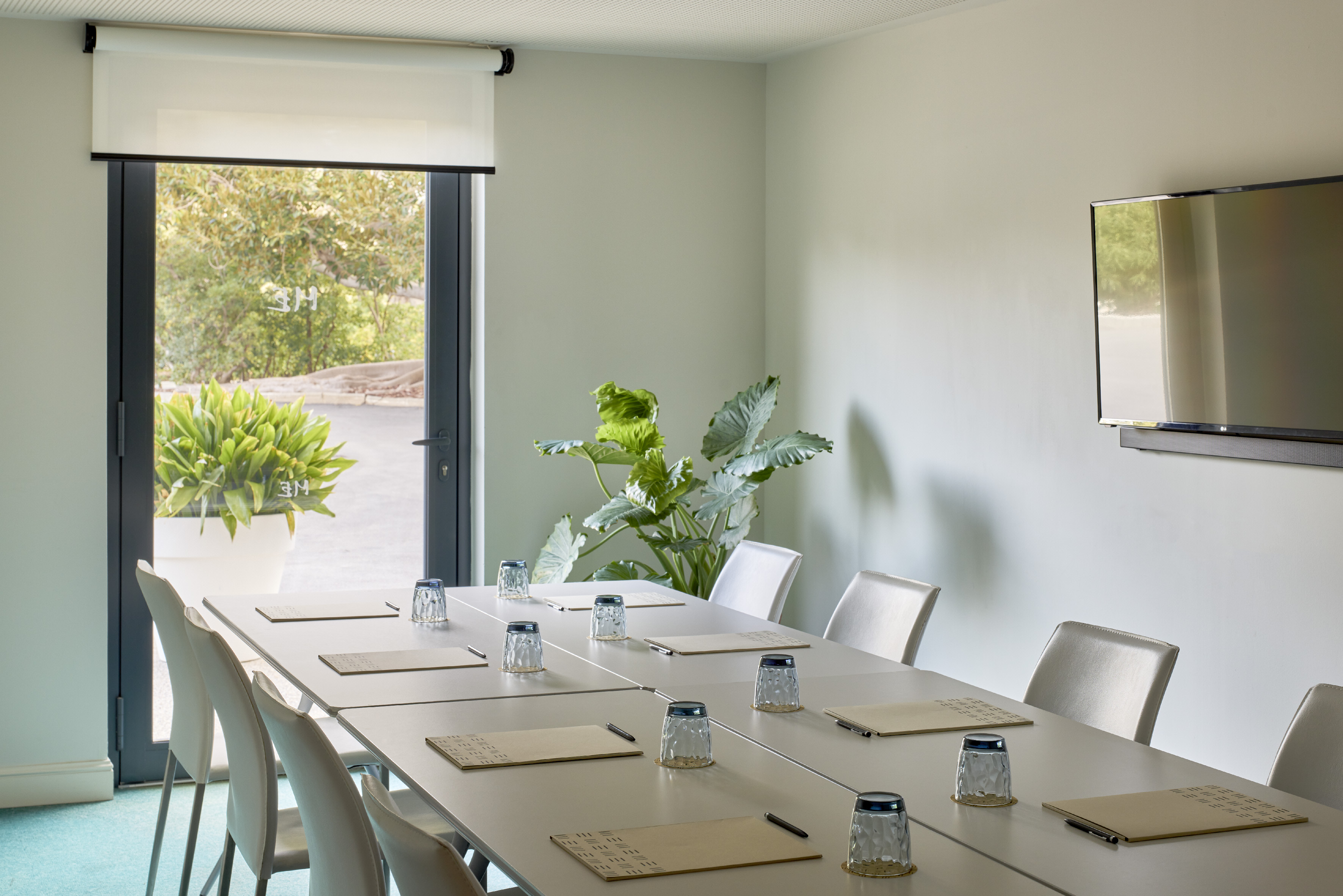 Modern conference room with table, chairs, wall-mounted TV, and outdoor view.
