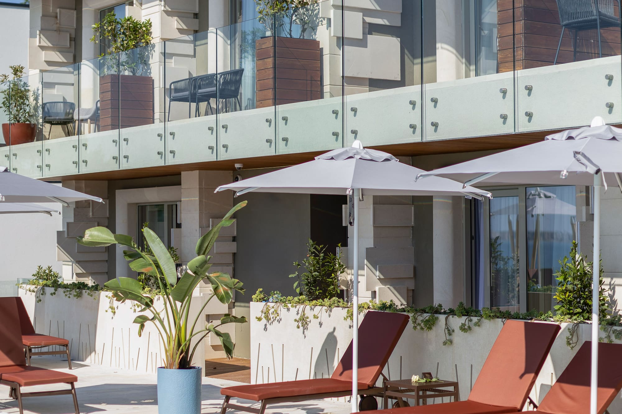 Resort swimming pool with sun loungers, umbrellas, and modern hotel balconies.
