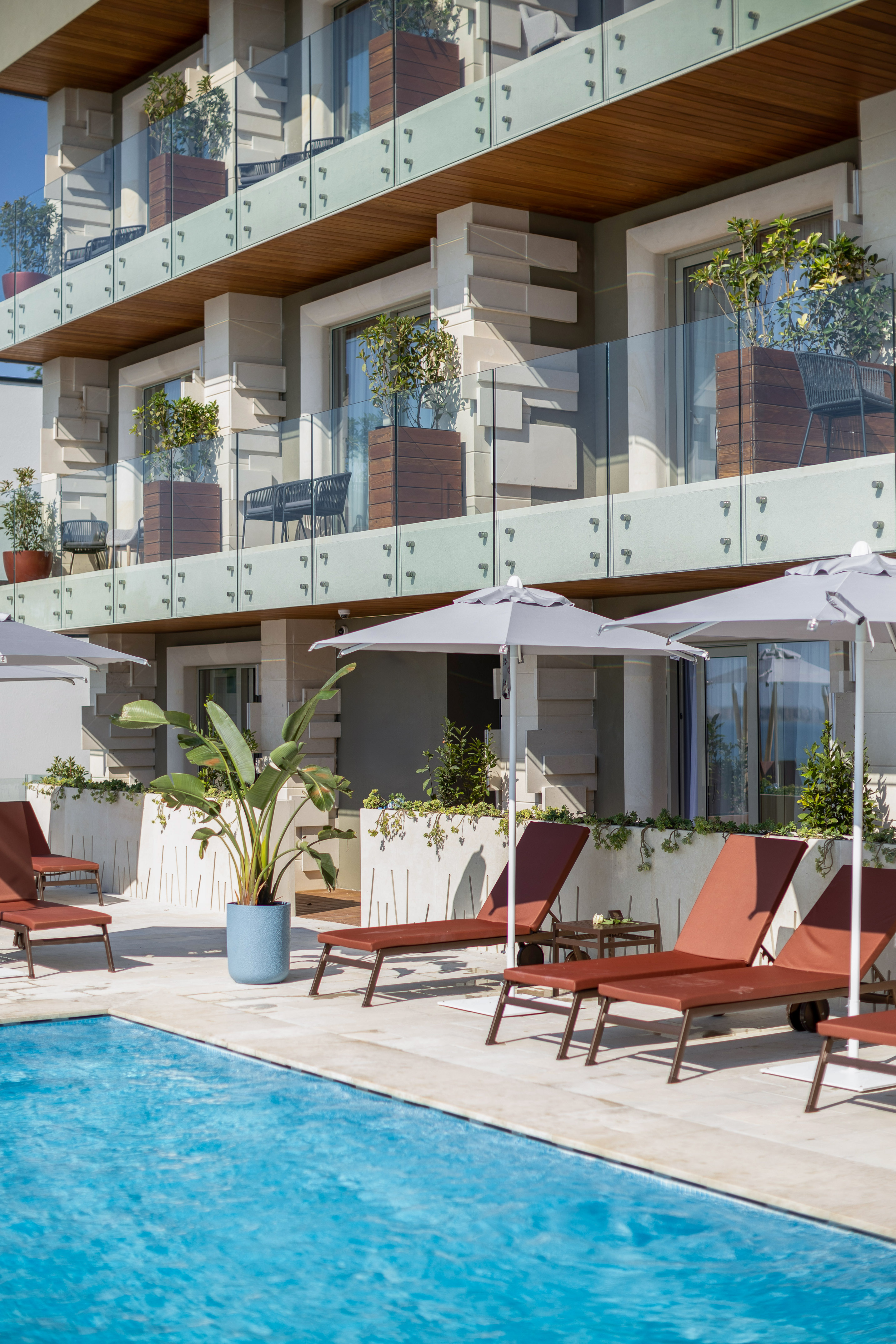 Resort swimming pool with sun loungers, umbrellas, and modern hotel balconies.