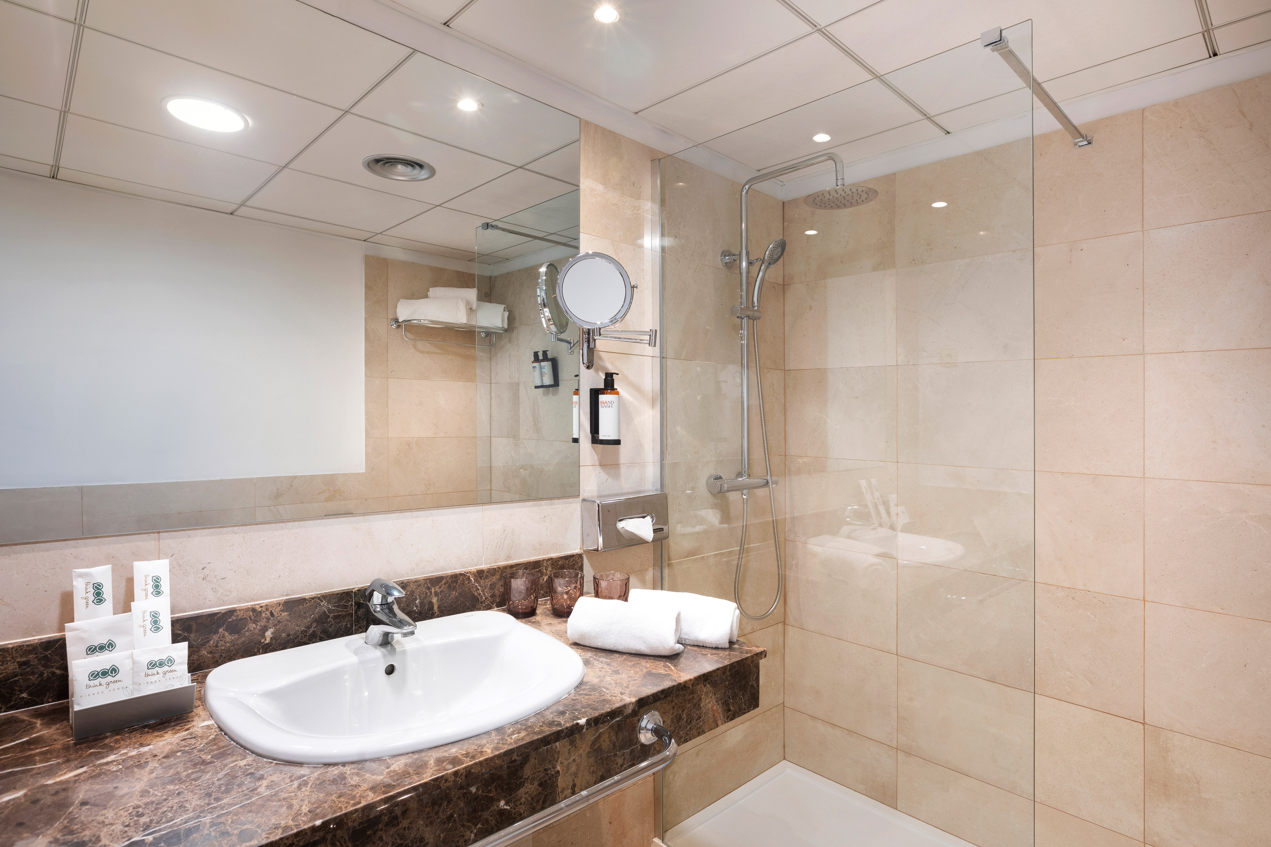 Modern hotel bathroom with marble vanity, white sink, mirror, and shower.