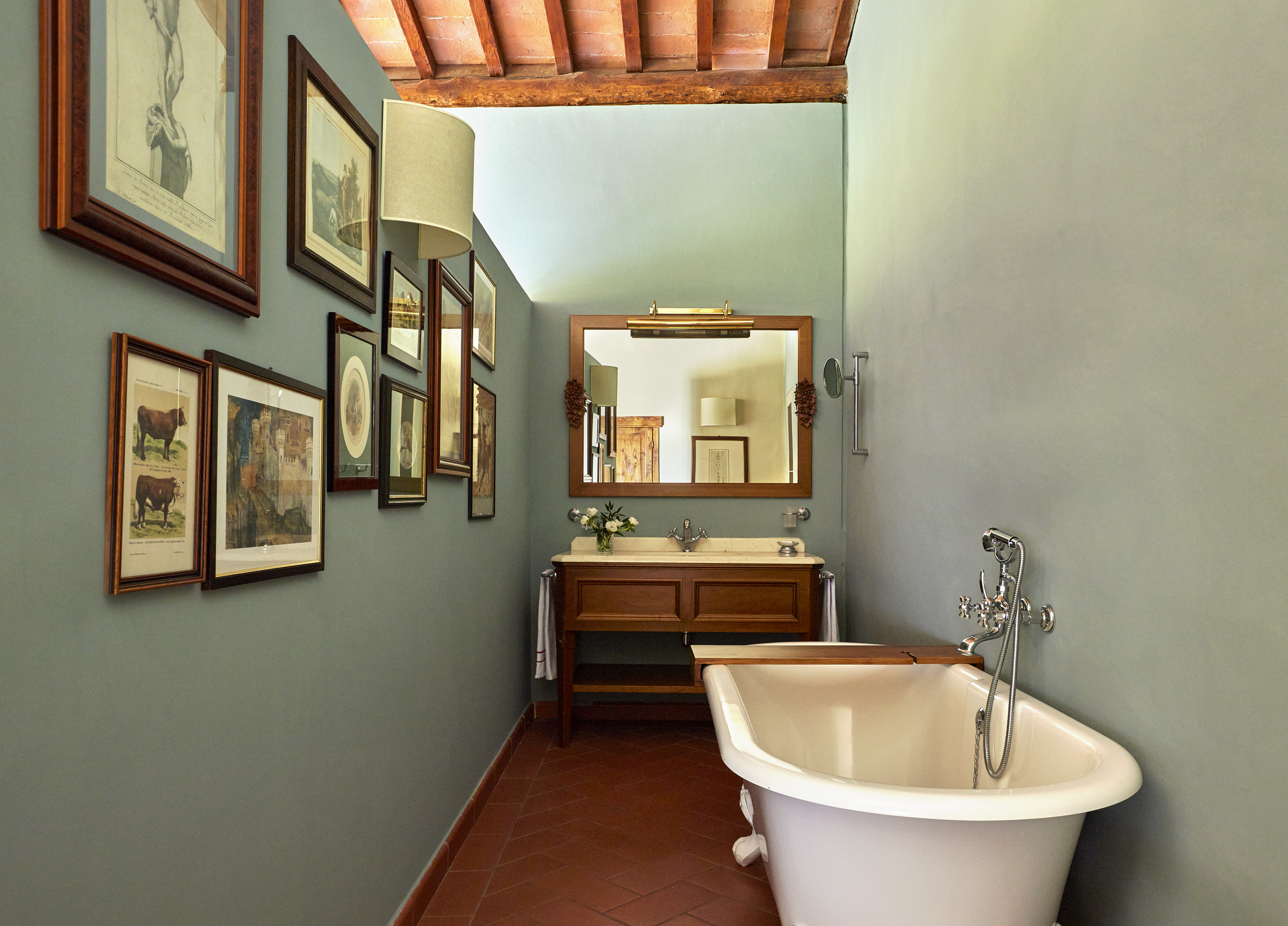 Rustic bathroom: clawfoot tub, wood vanity, framed art, and terracotta floor.
