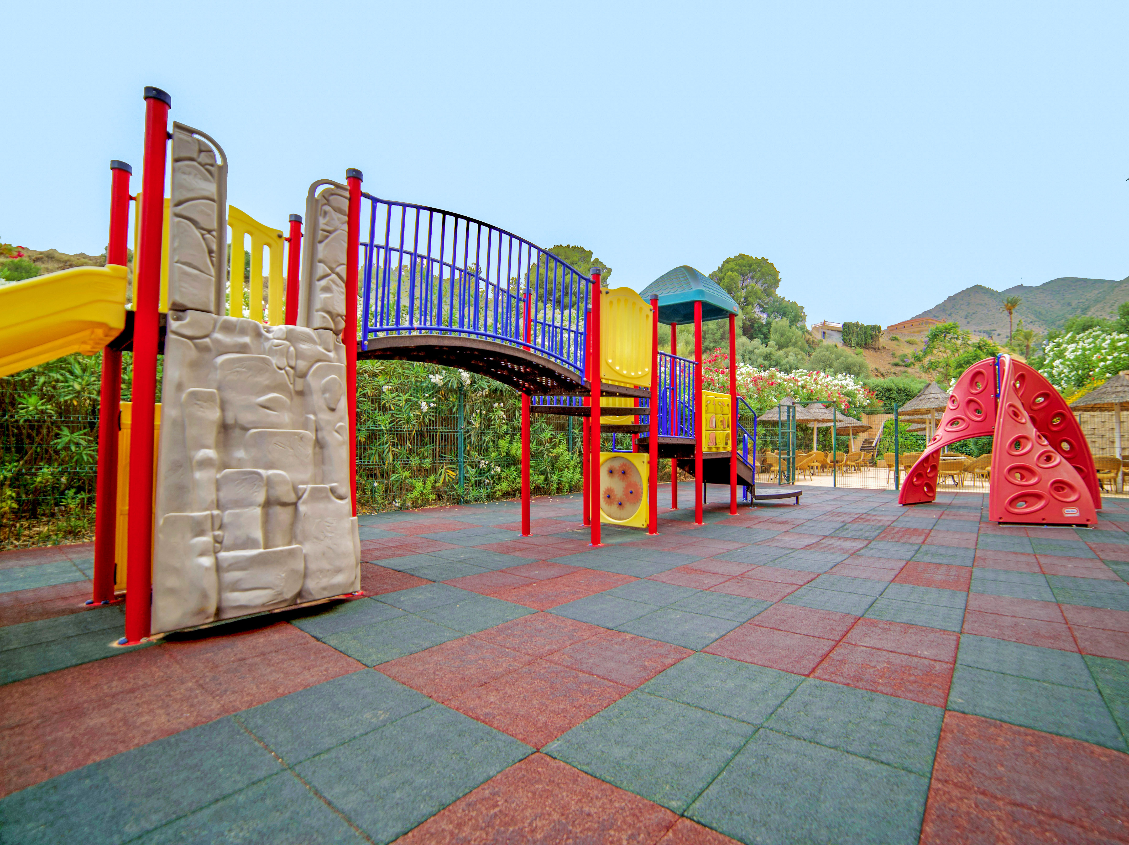 Colorful outdoor playground with slides, climbing elements, and rubber floor.