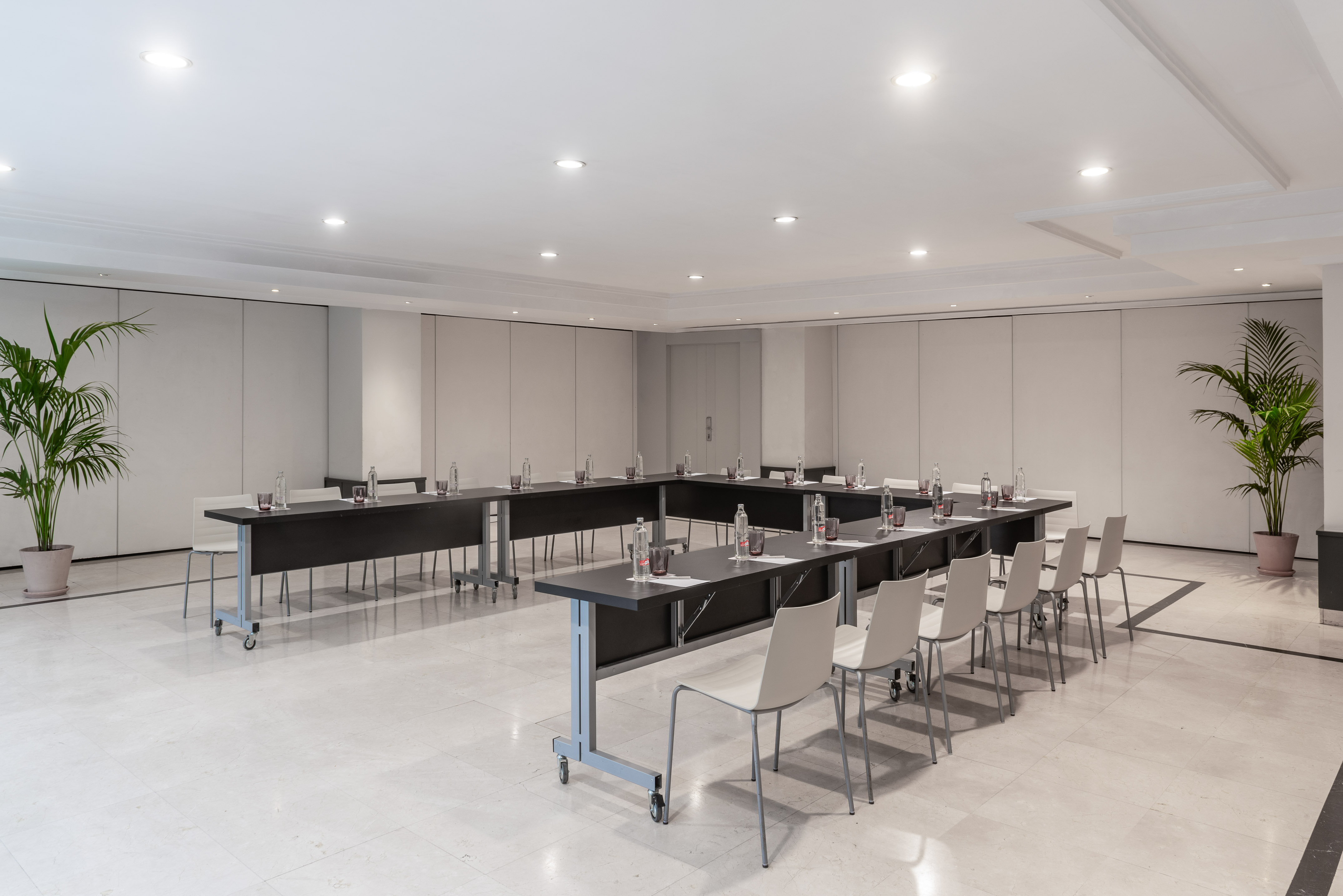 Modern U-shaped conference room setup with chairs, tables, and potted plants.
