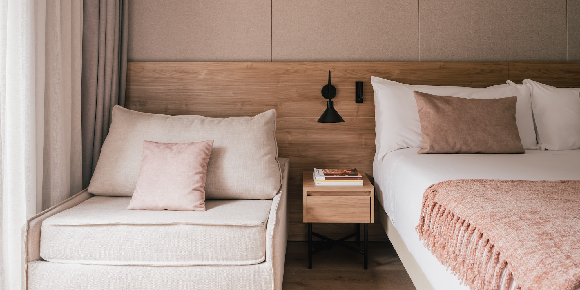 Modern bedroom with bed, chaise lounge, wooden headboard, and pink accents.