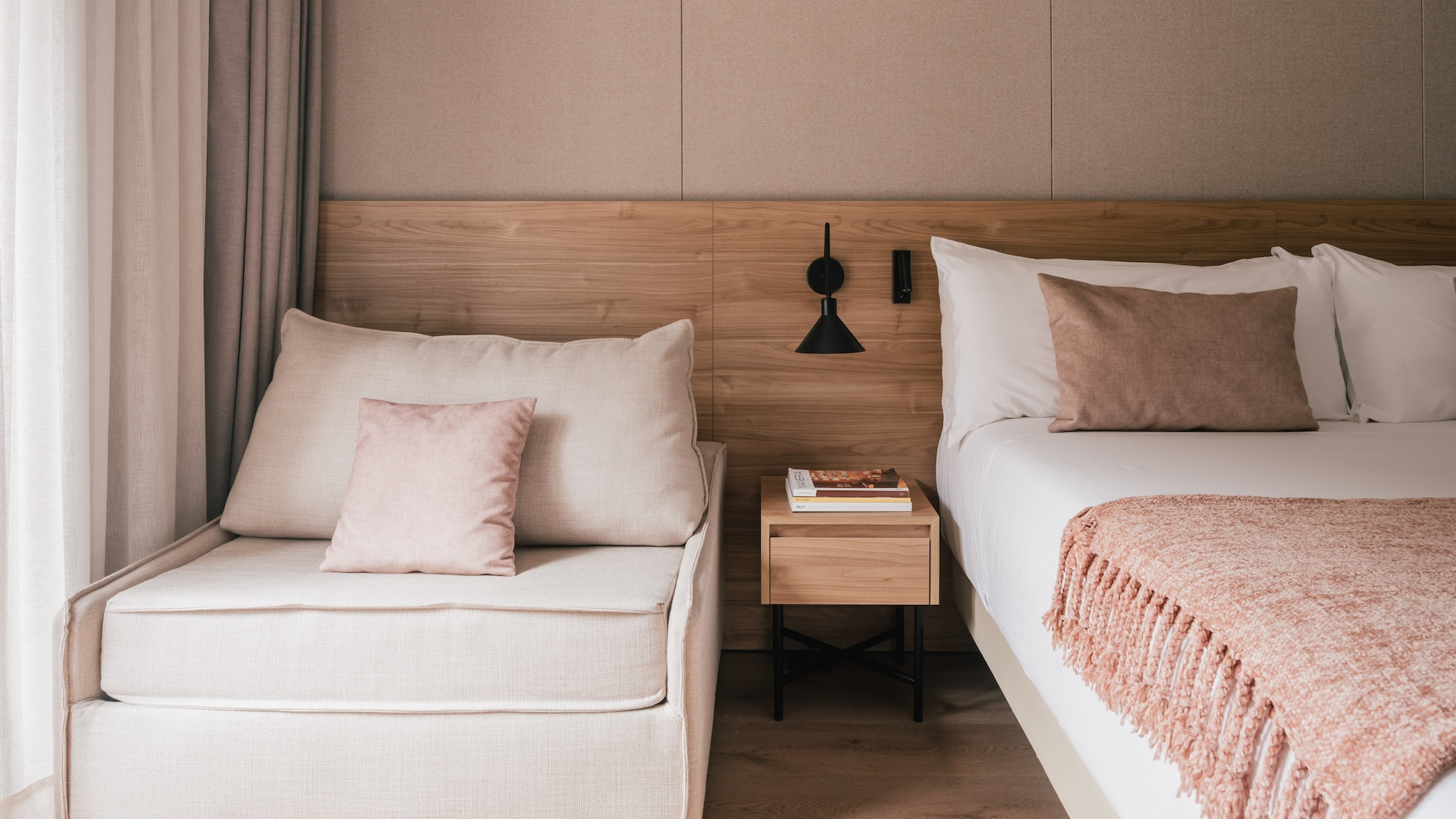 Modern bedroom with bed, chaise lounge, wooden headboard, and pink accents.