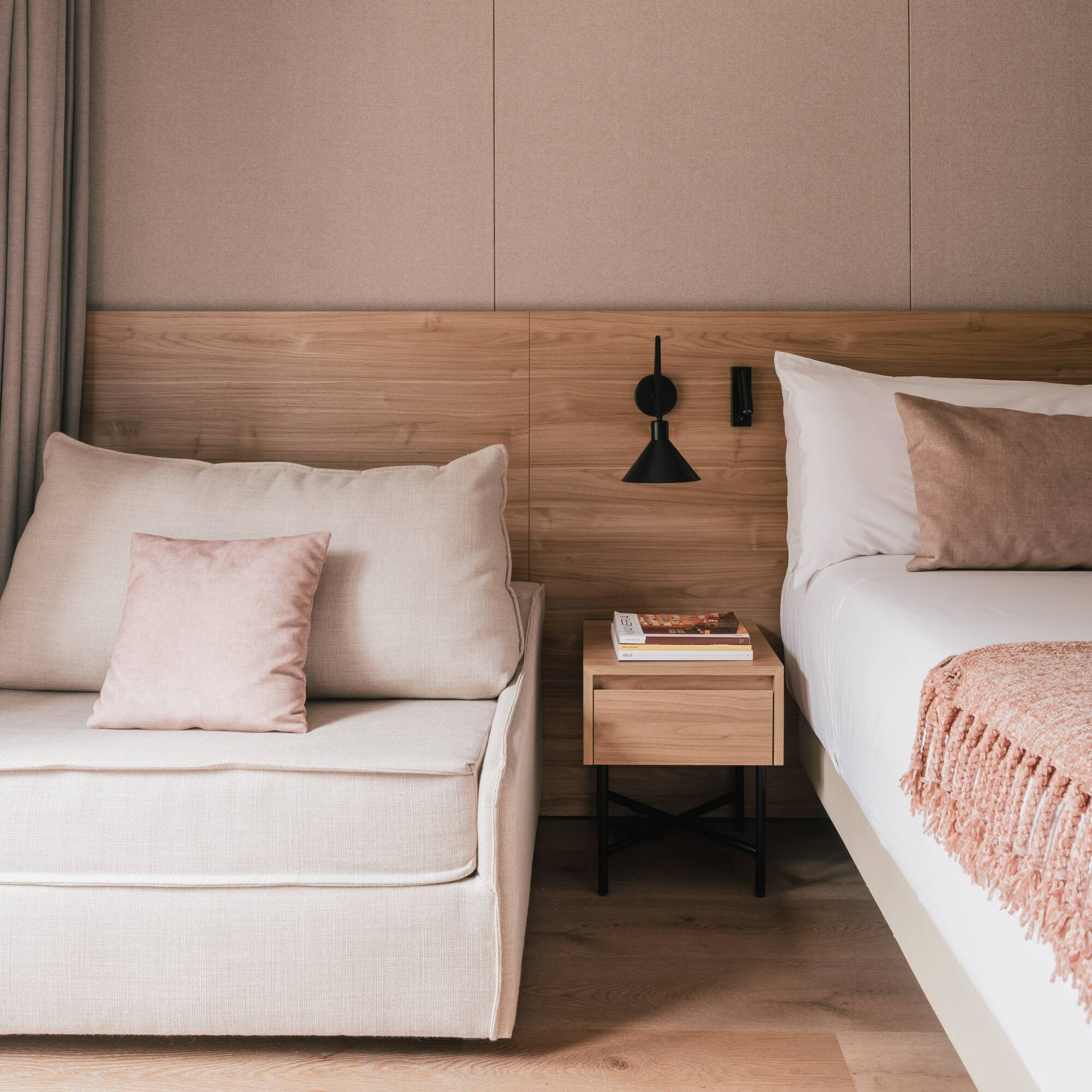 Modern bedroom with bed, chaise lounge, wooden headboard, and pink accents.