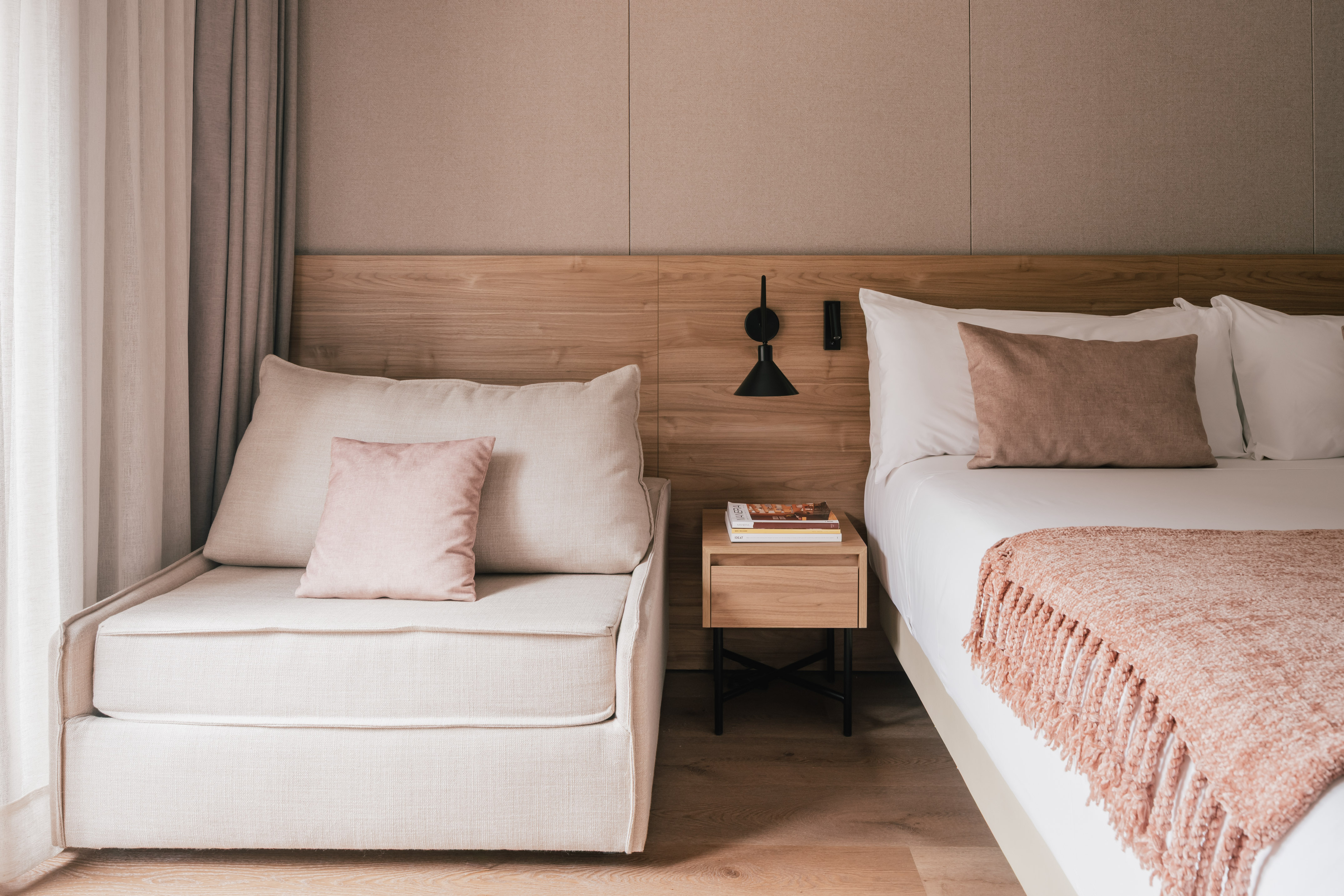 Modern bedroom with bed, chaise lounge, wooden headboard, and pink accents.