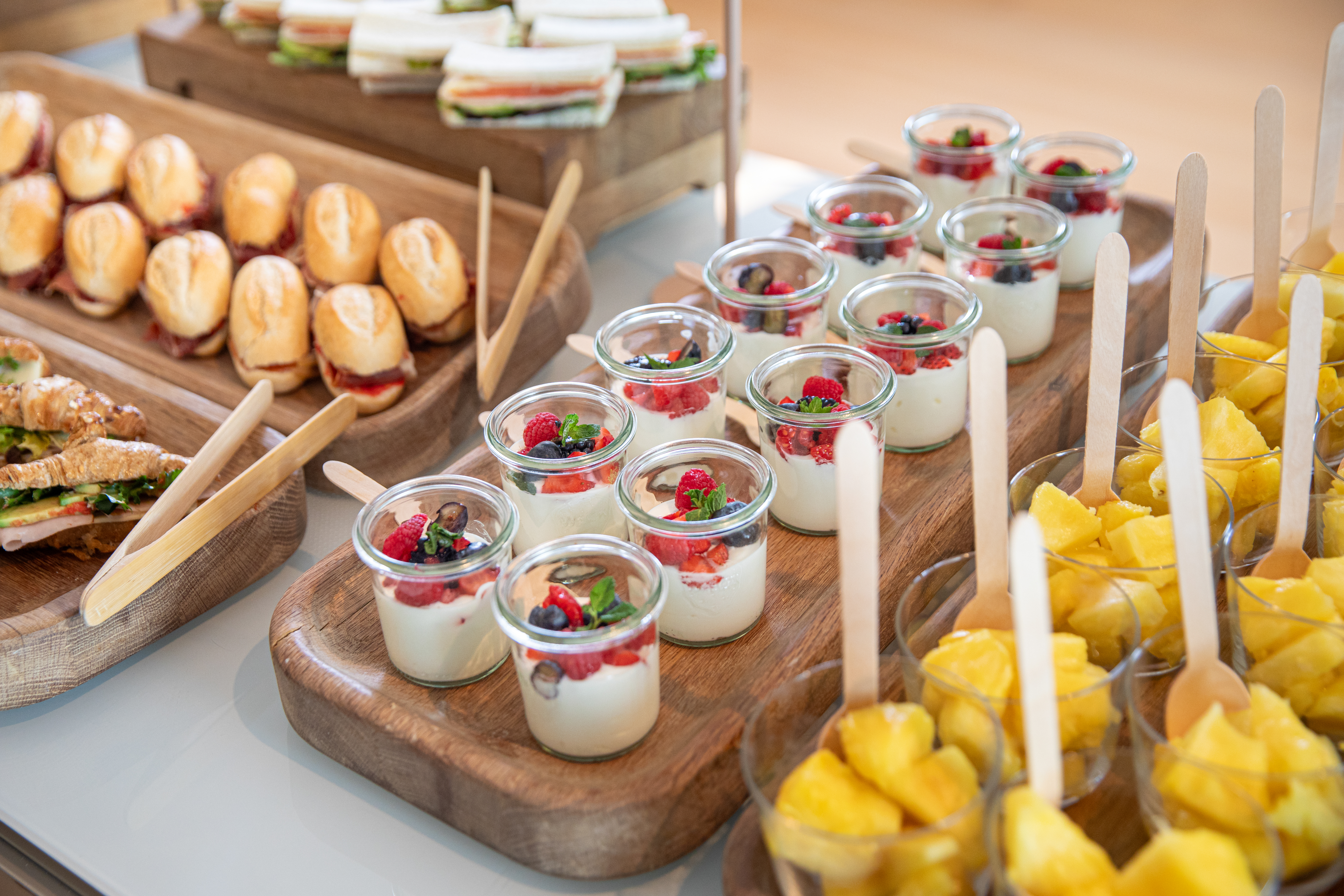 Catering buffet with mini sandwiches, berry parfaits, and pineapple cups.