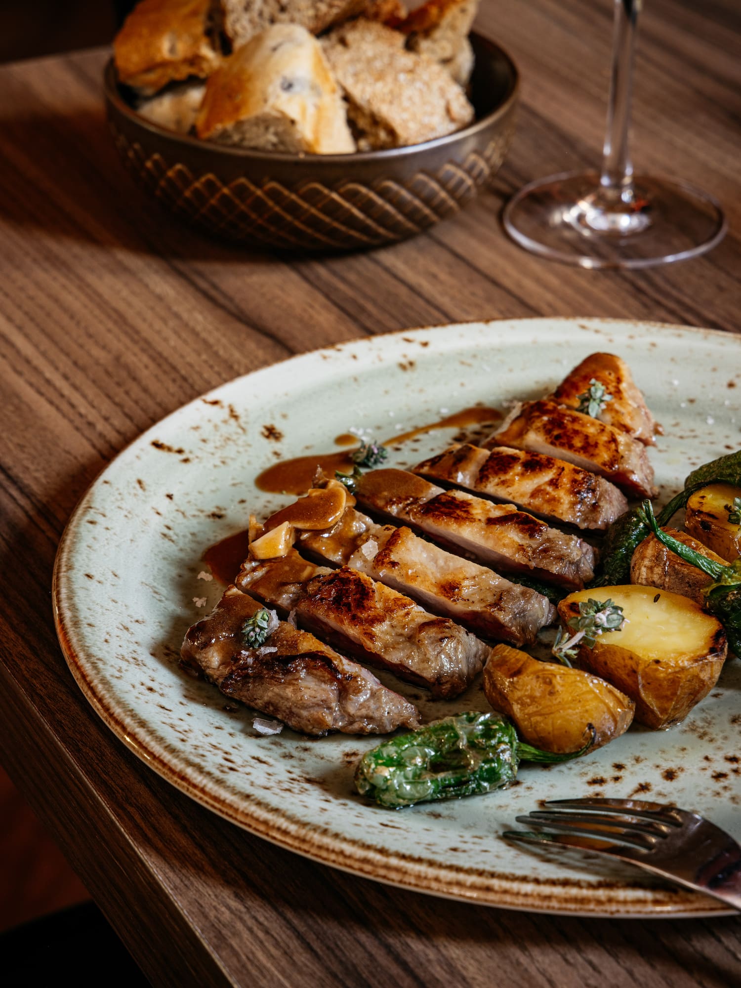 Cena gourmet: Carne asada, patatas y pimientos en plato sobre madera, con pan.