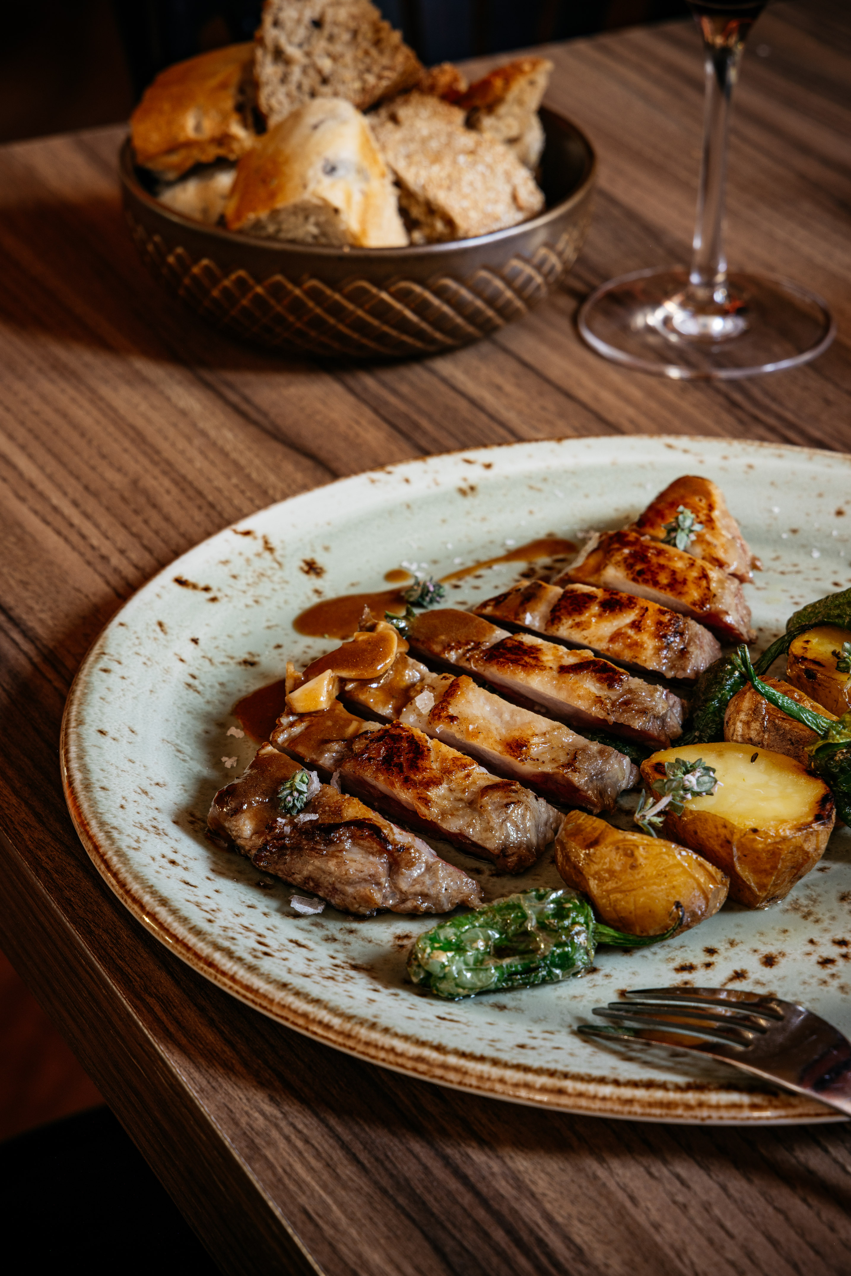 Cena gourmet: Carne asada, patatas y pimientos en plato sobre madera, con pan.