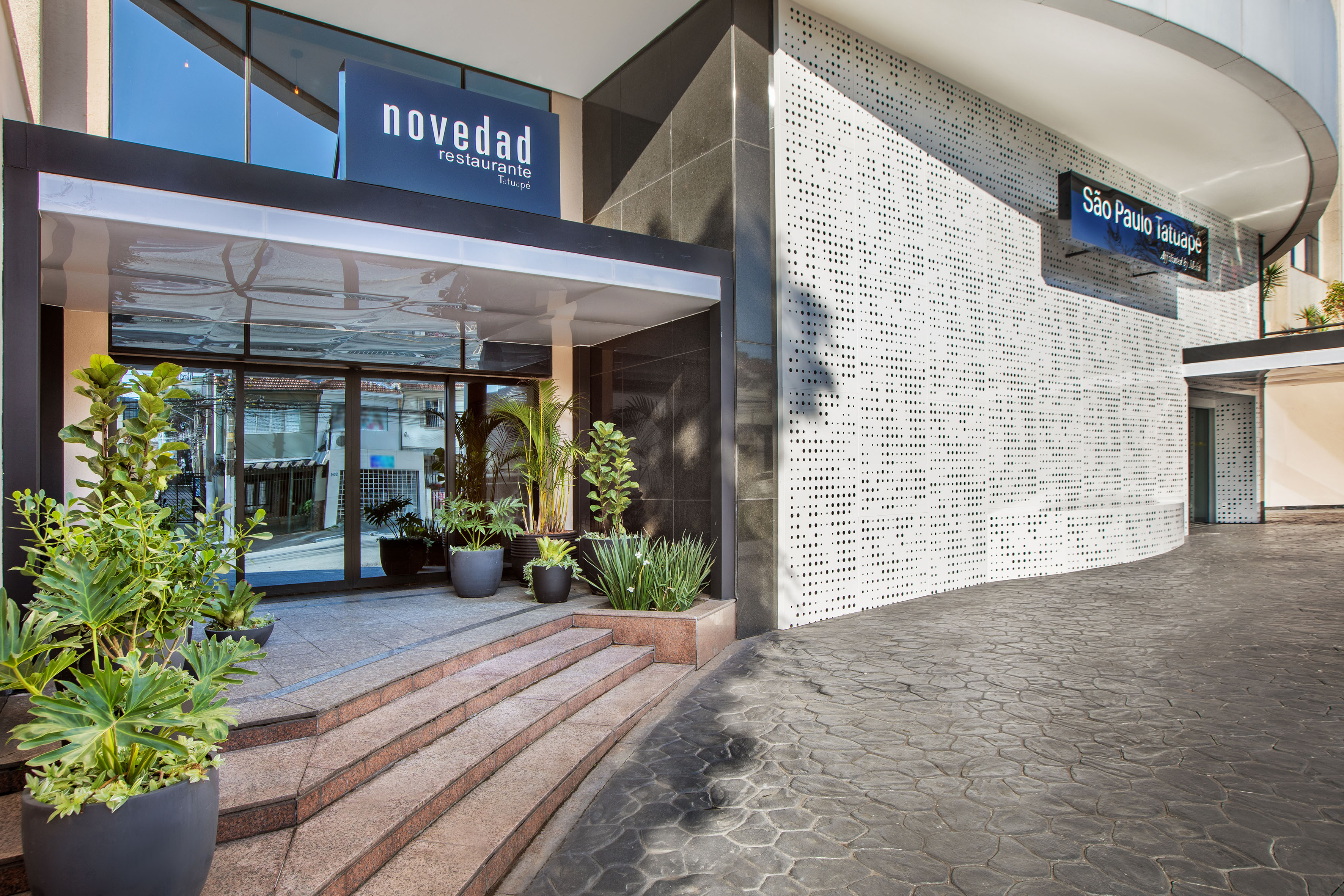 Novedad Restaurante Tatuapé entrance. Modern building with stairs and potted plants.