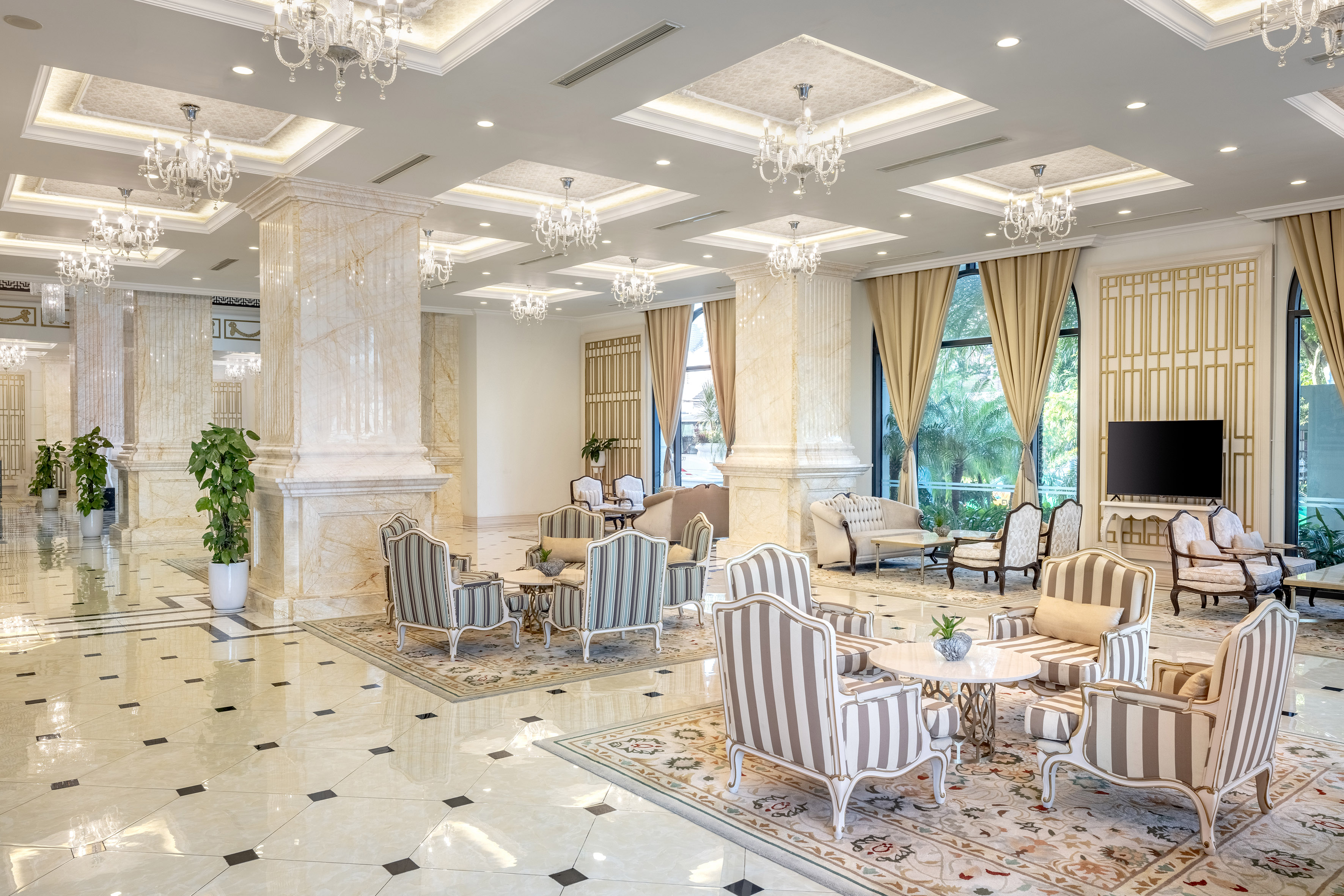Elegant hotel lobby with marble pillars, ornate chandeliers, and striped lounge seating.