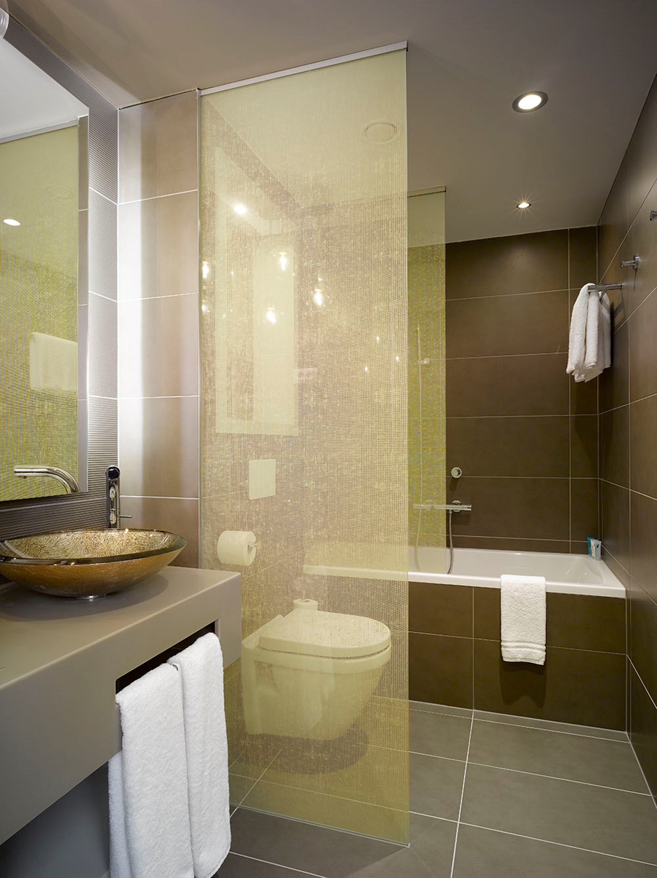 Modern bathroom with glass partition, vessel sink, brown tiles, and bathtub.