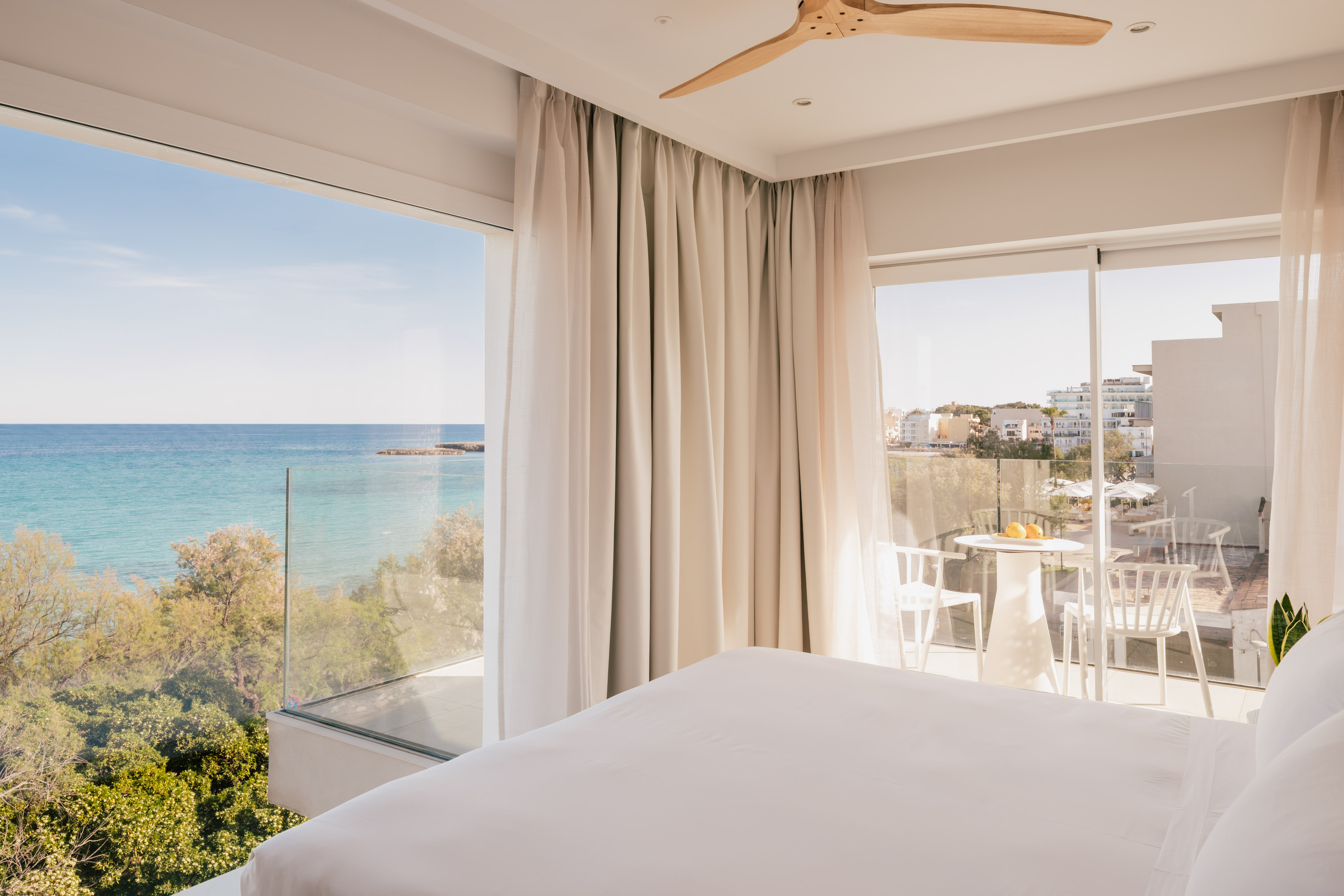 Habitación moderna de hotel con balcón, cama blanca y vista al mar Mediterráneo.