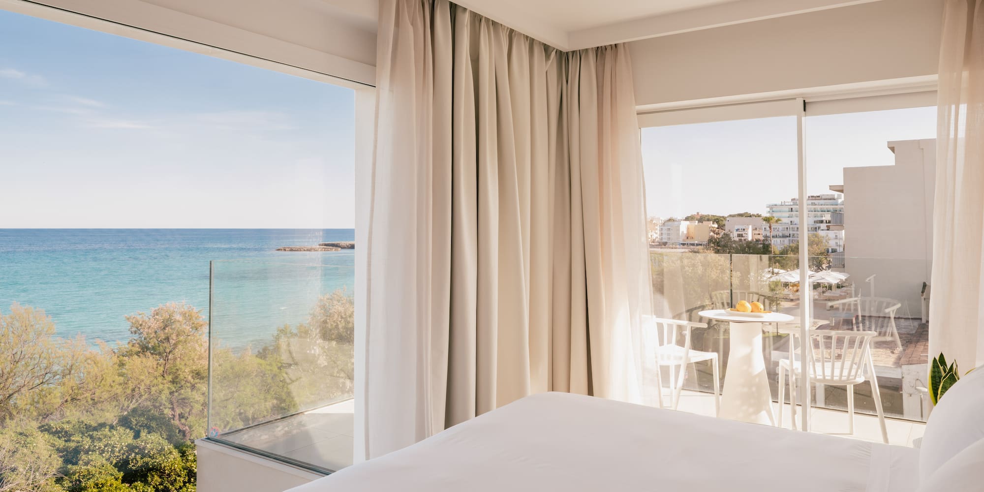 Modern hotel bedroom with panoramic sea view, private balcony, and white bed.