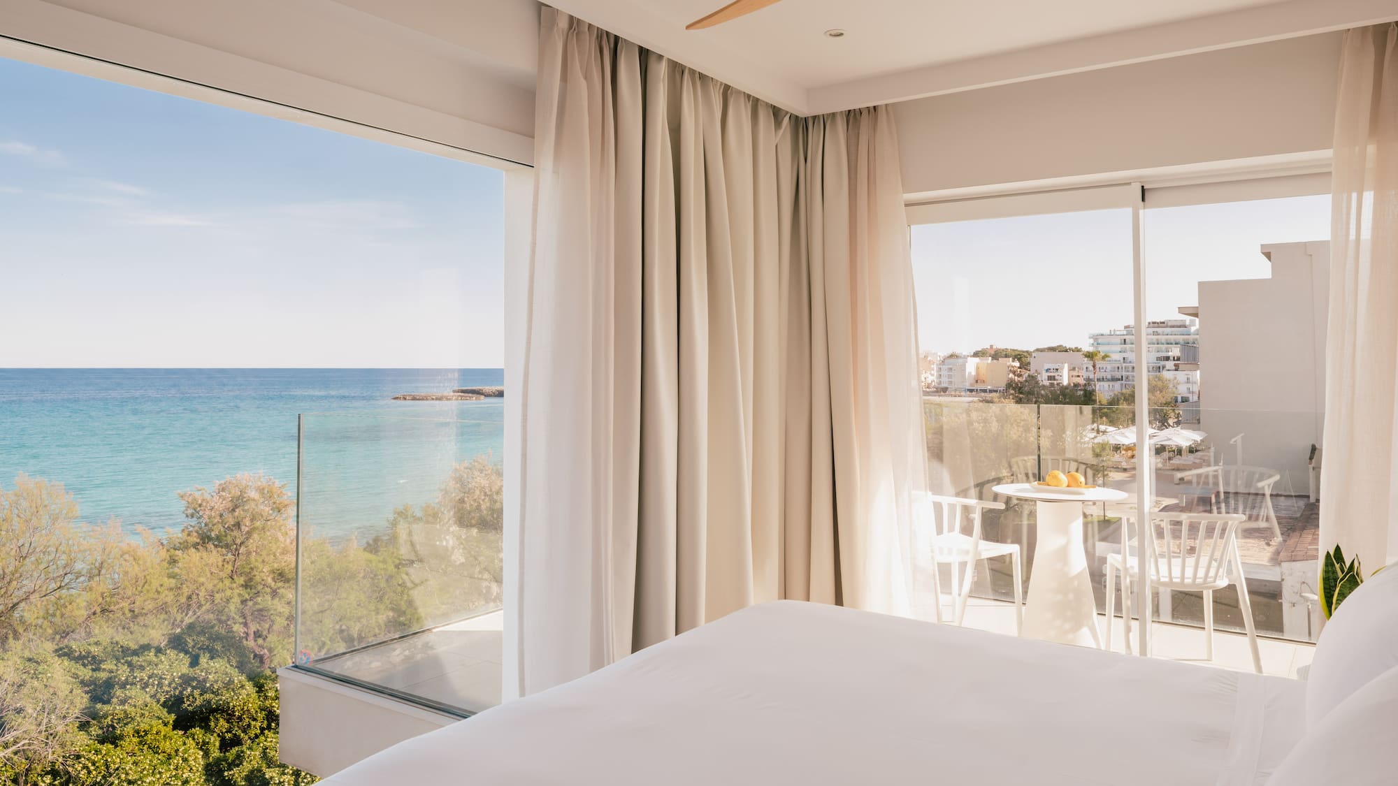 Modern hotel bedroom with panoramic sea view, private balcony, and white bed.
