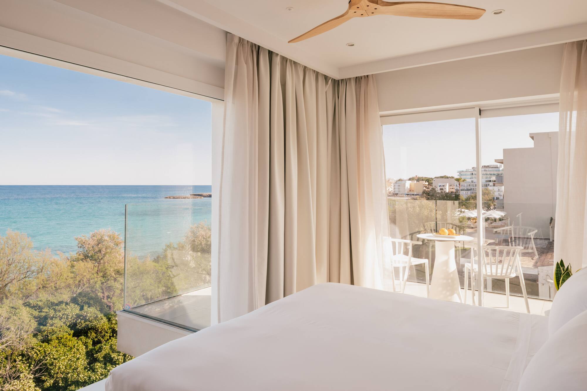 Habitación moderna de hotel con balcón, cama blanca y vista al mar Mediterráneo.