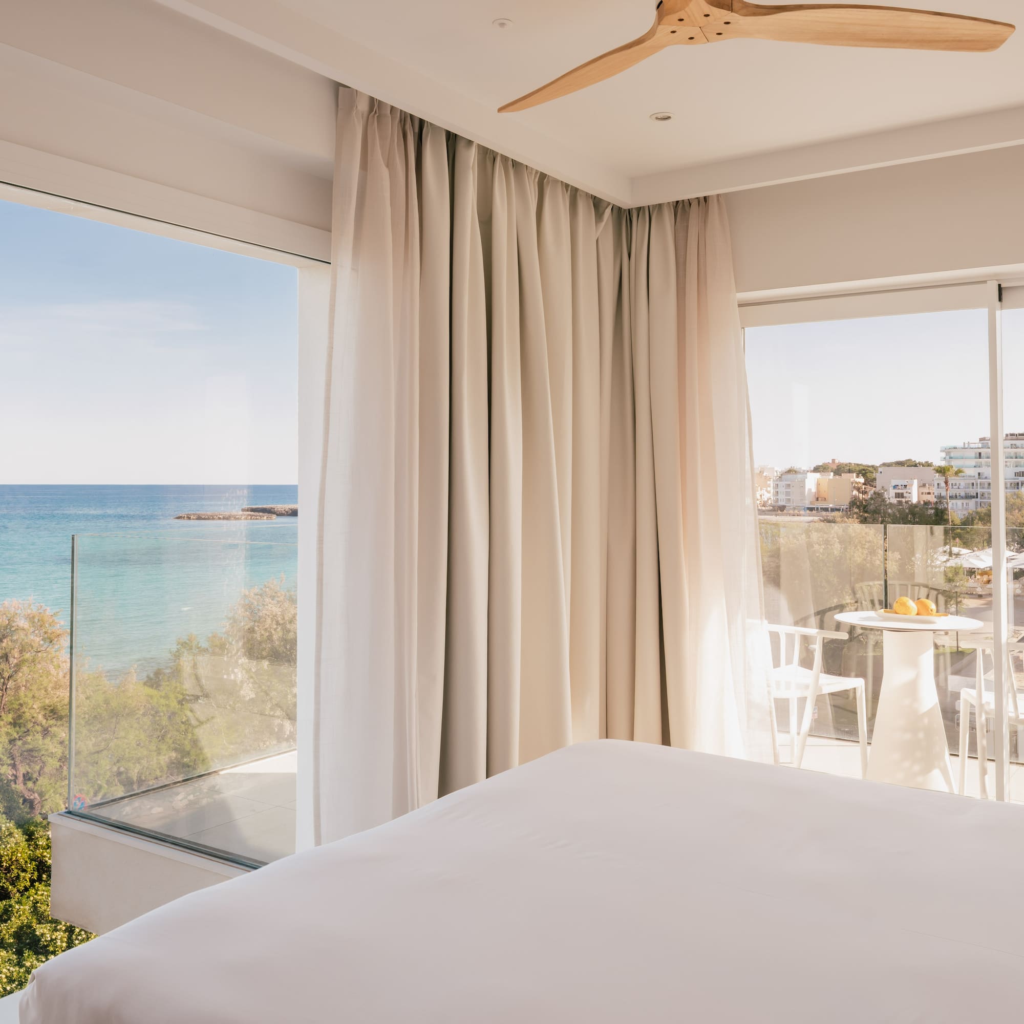 Modern hotel bedroom with panoramic sea view, private balcony, and white bed.