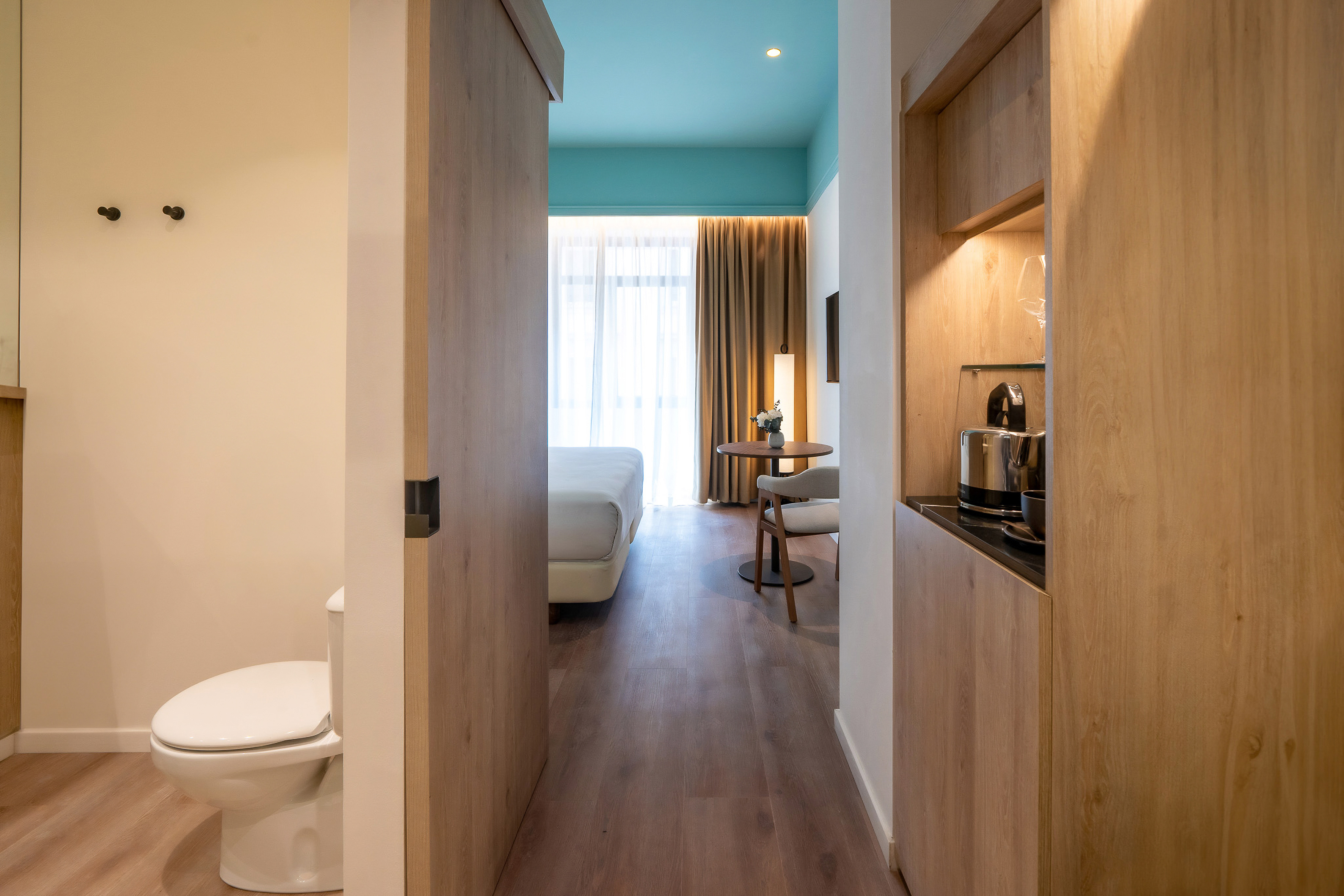 Modern hotel room with blue ceiling, bedroom, coffee station, and toilet.