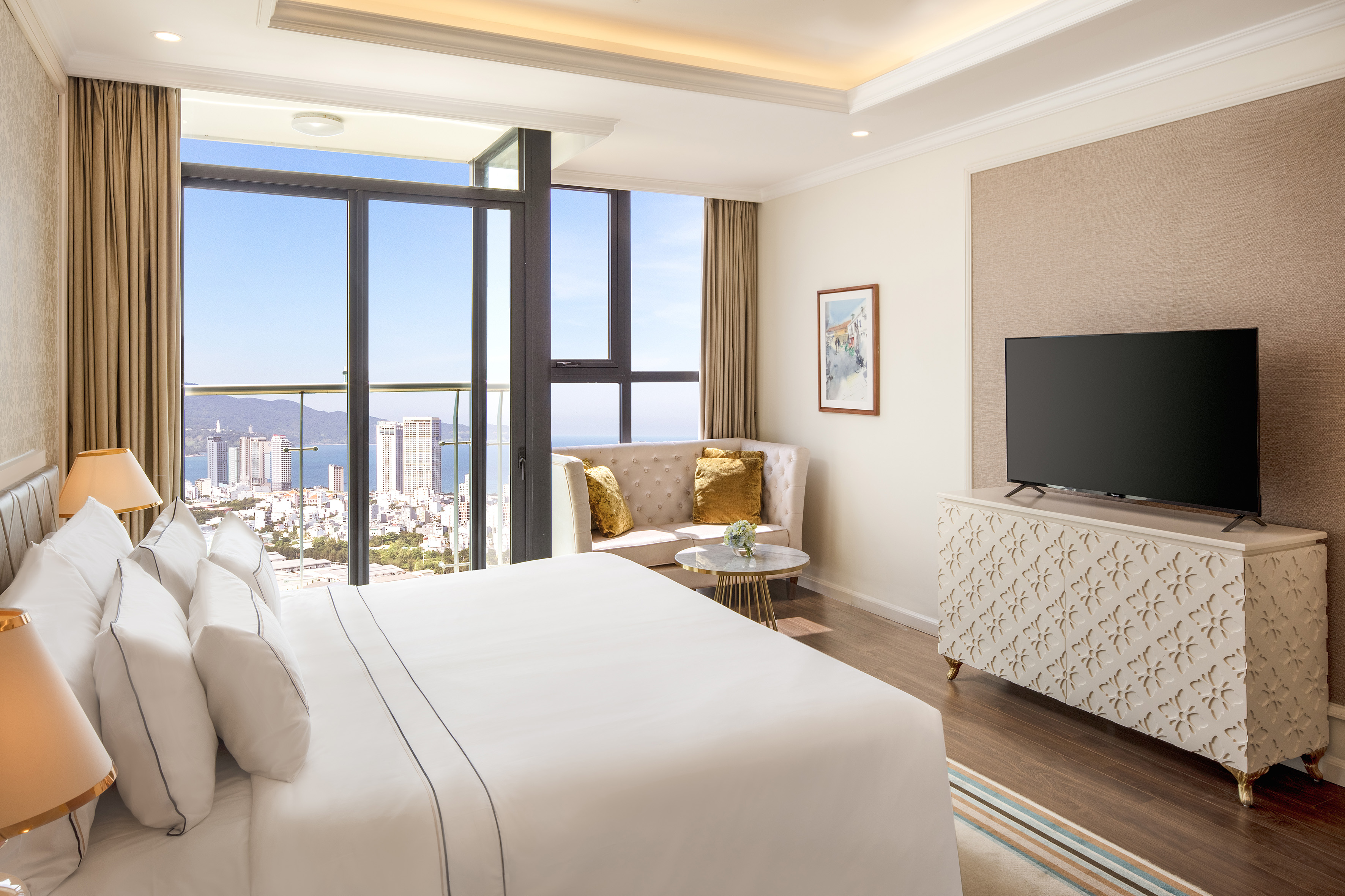 Modern hotel room with king bed, TV, and panoramic city and ocean view.