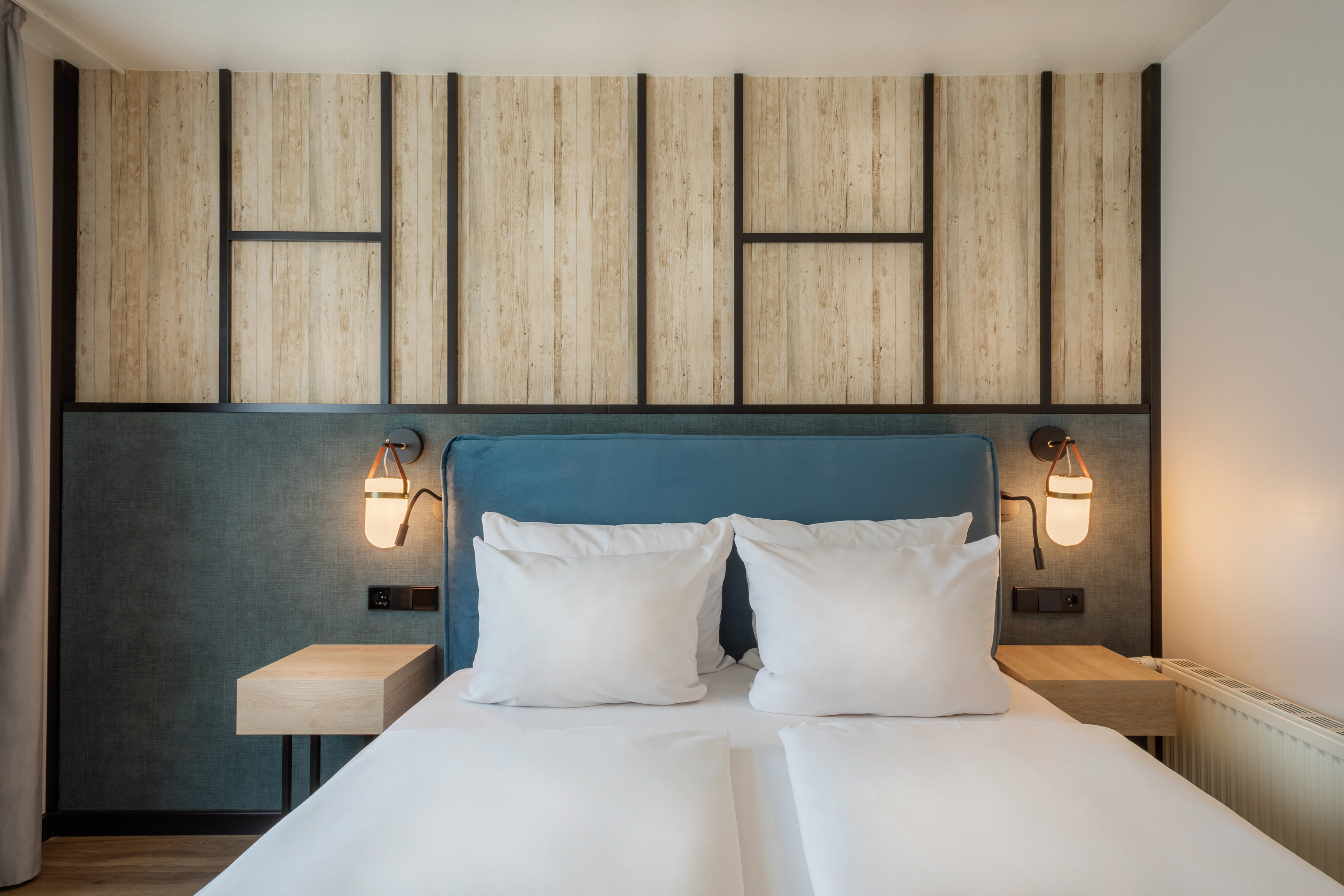 Modern hotel bedroom with blue headboard, wood panels, nightstands, warm lights.
