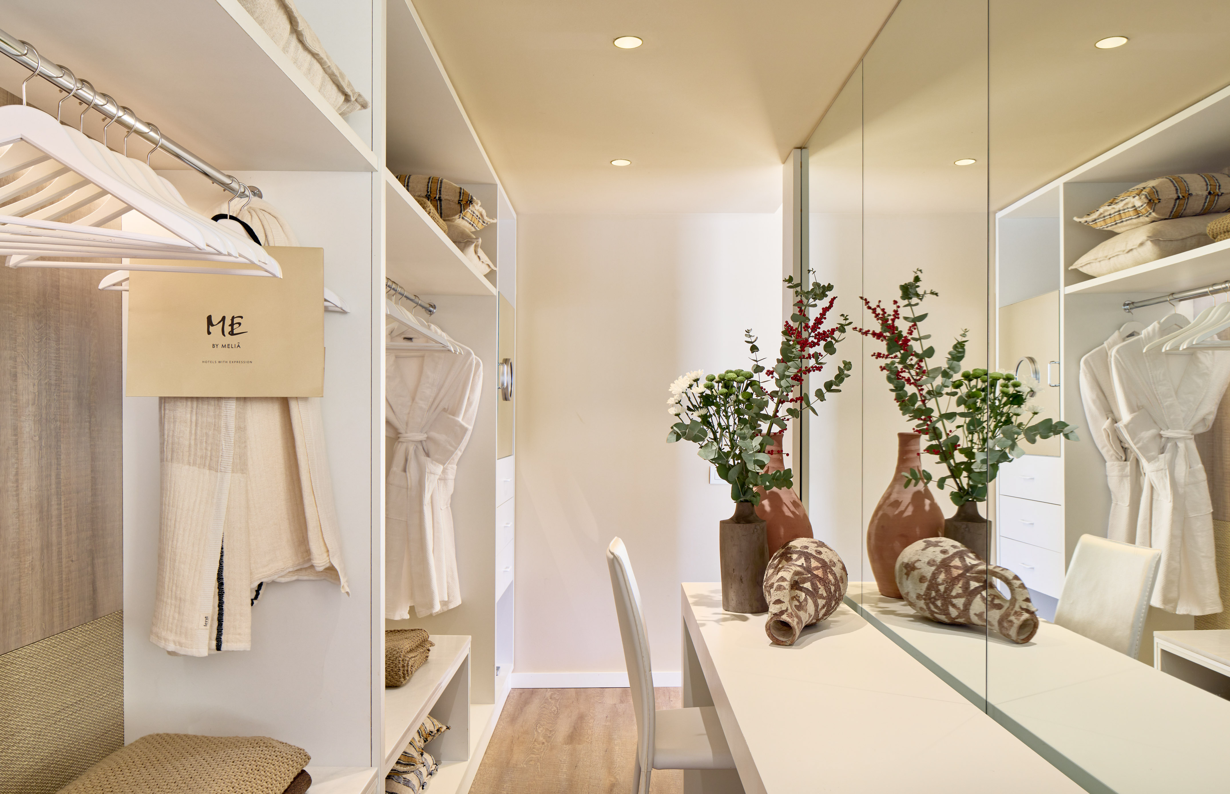 ME by Meliã hotel walk-in closet with white shelves, mirror vanity, robes.