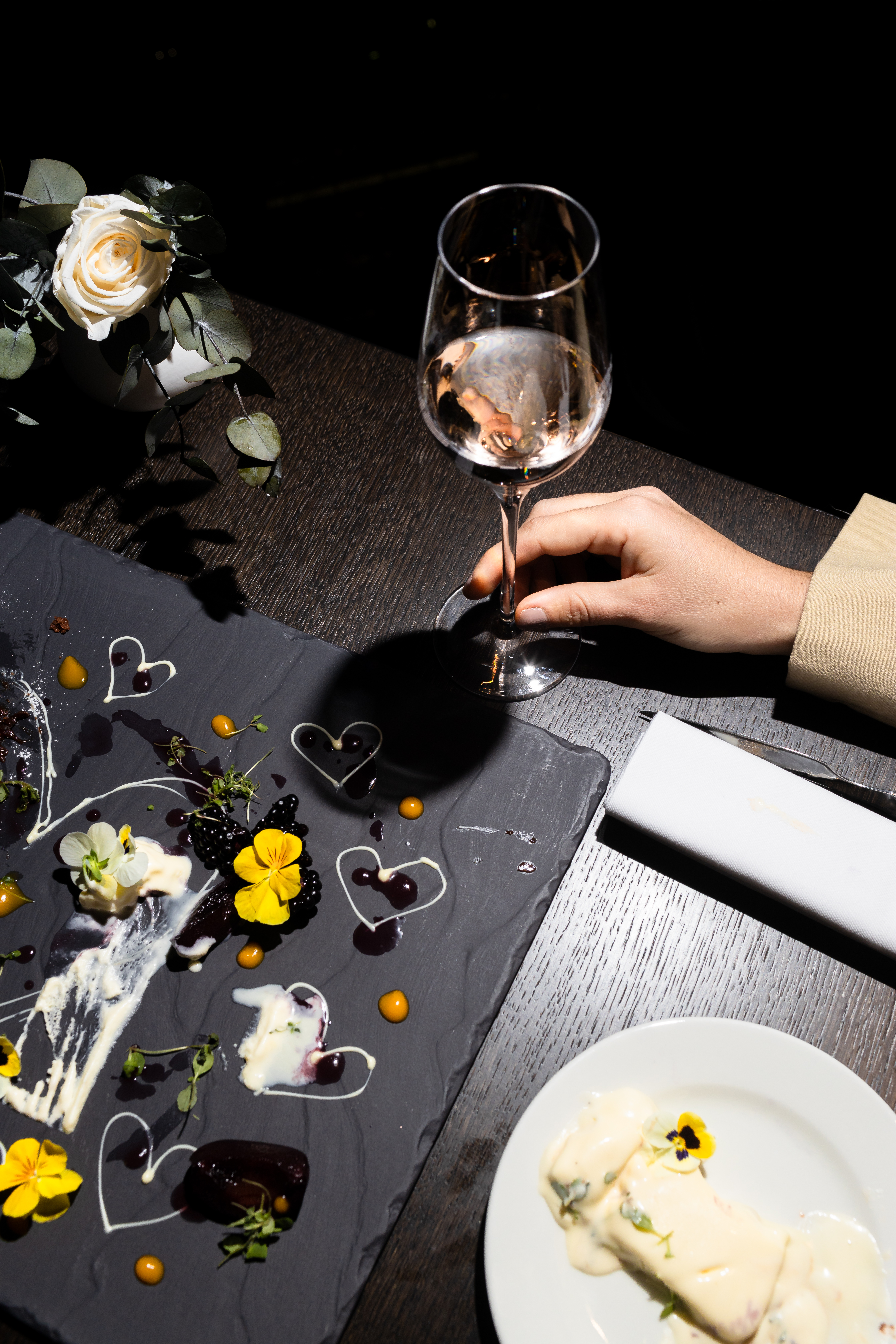 Elegant dessert platter featuring berries, pansies, cream hearts, and a wine glass.