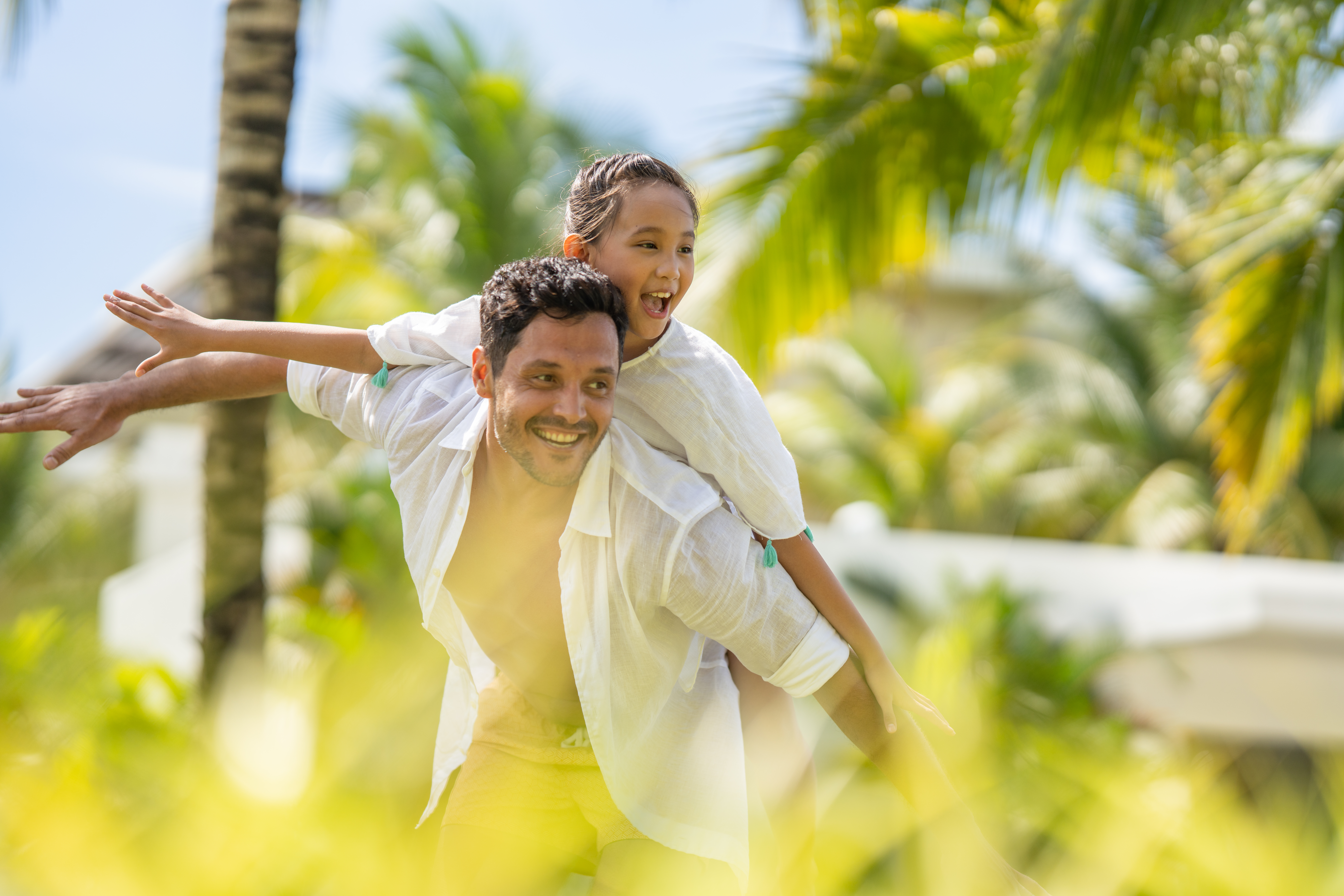 Happy father and daughter on piggyback ride at tropical resort.