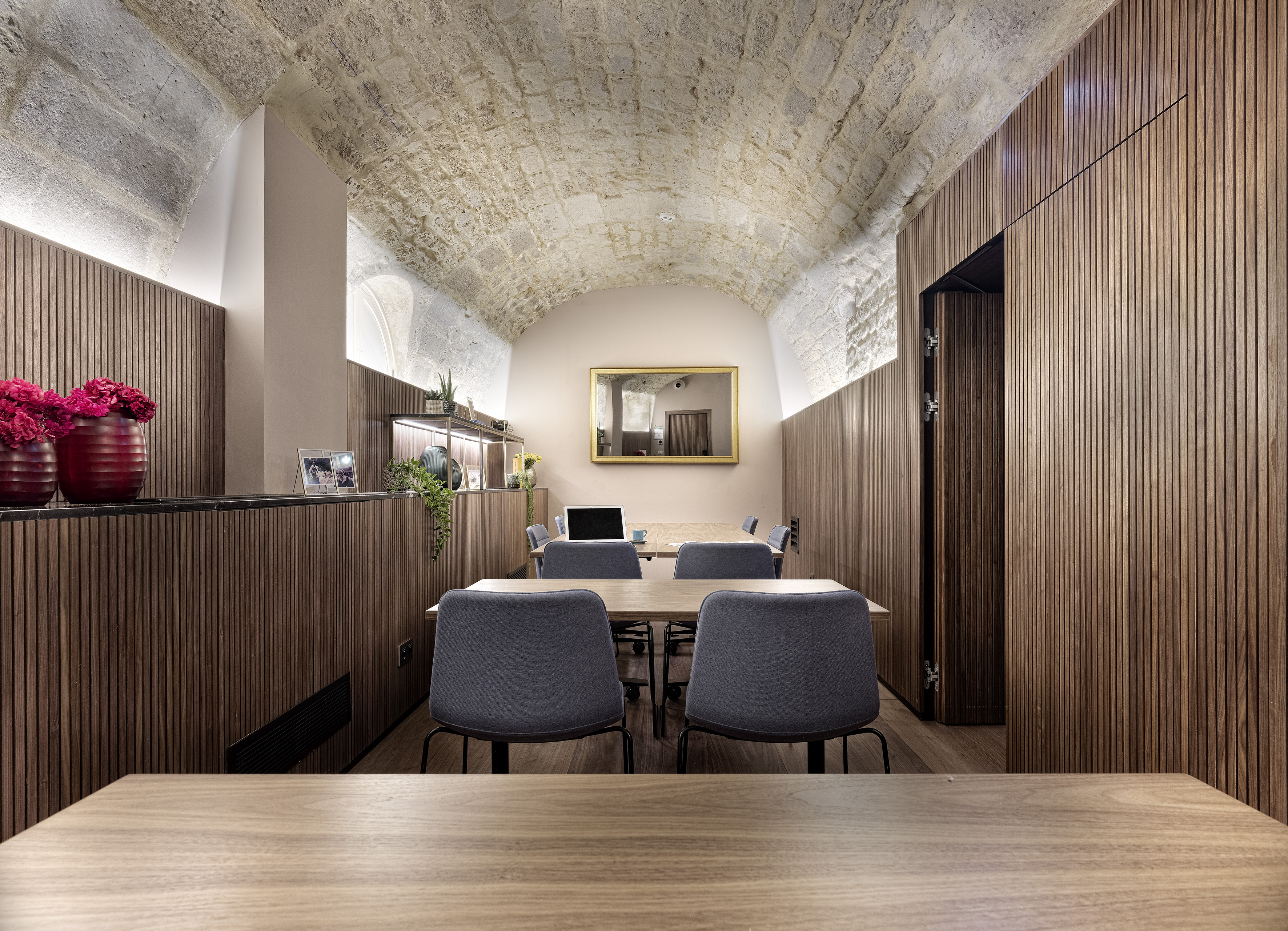 Modern workspace with vaulted stone ceiling, wood paneling, and conference tables.