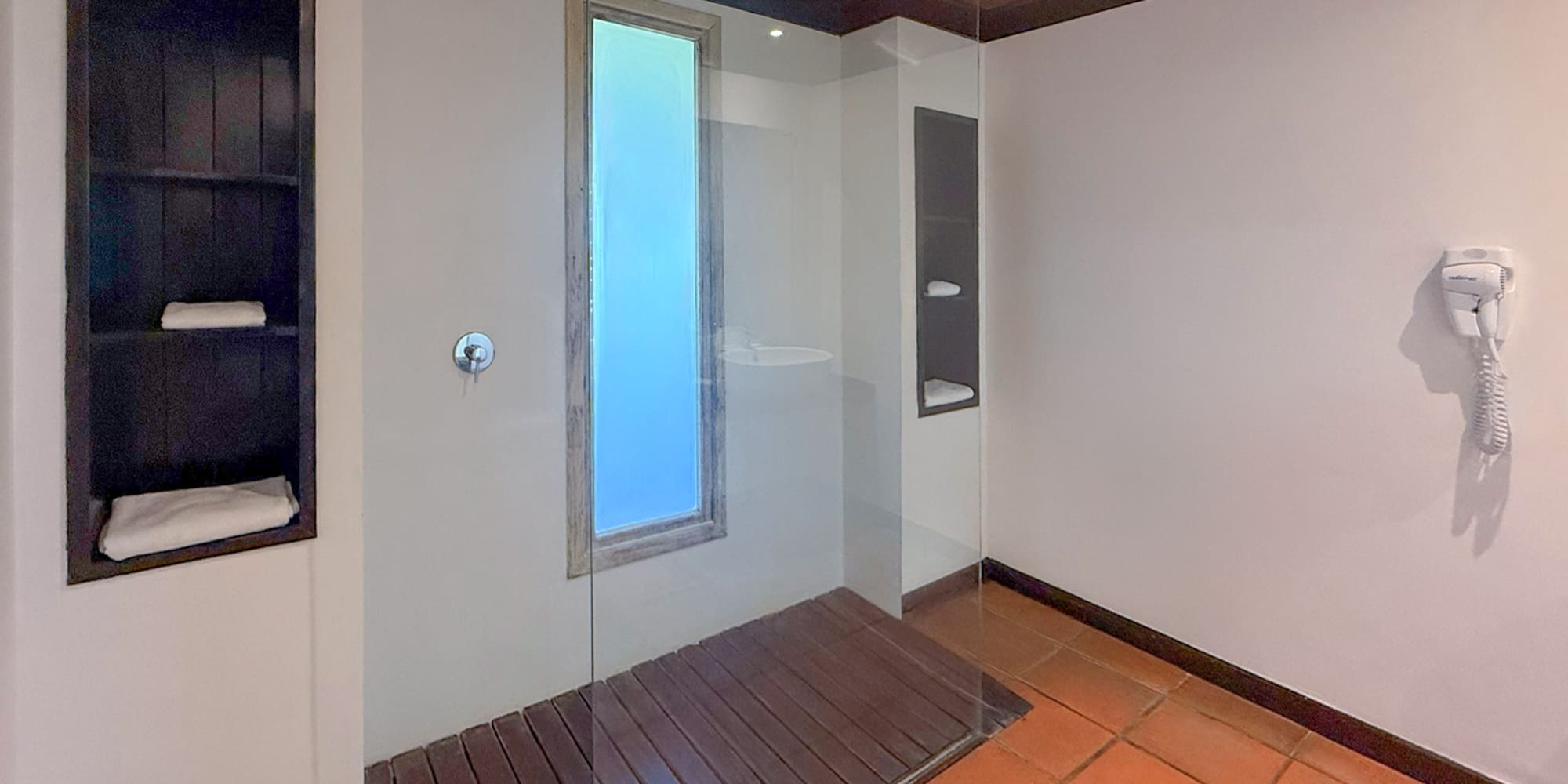 Modern bathroom with glass walk-in shower, wood floor, terracotta tiles.