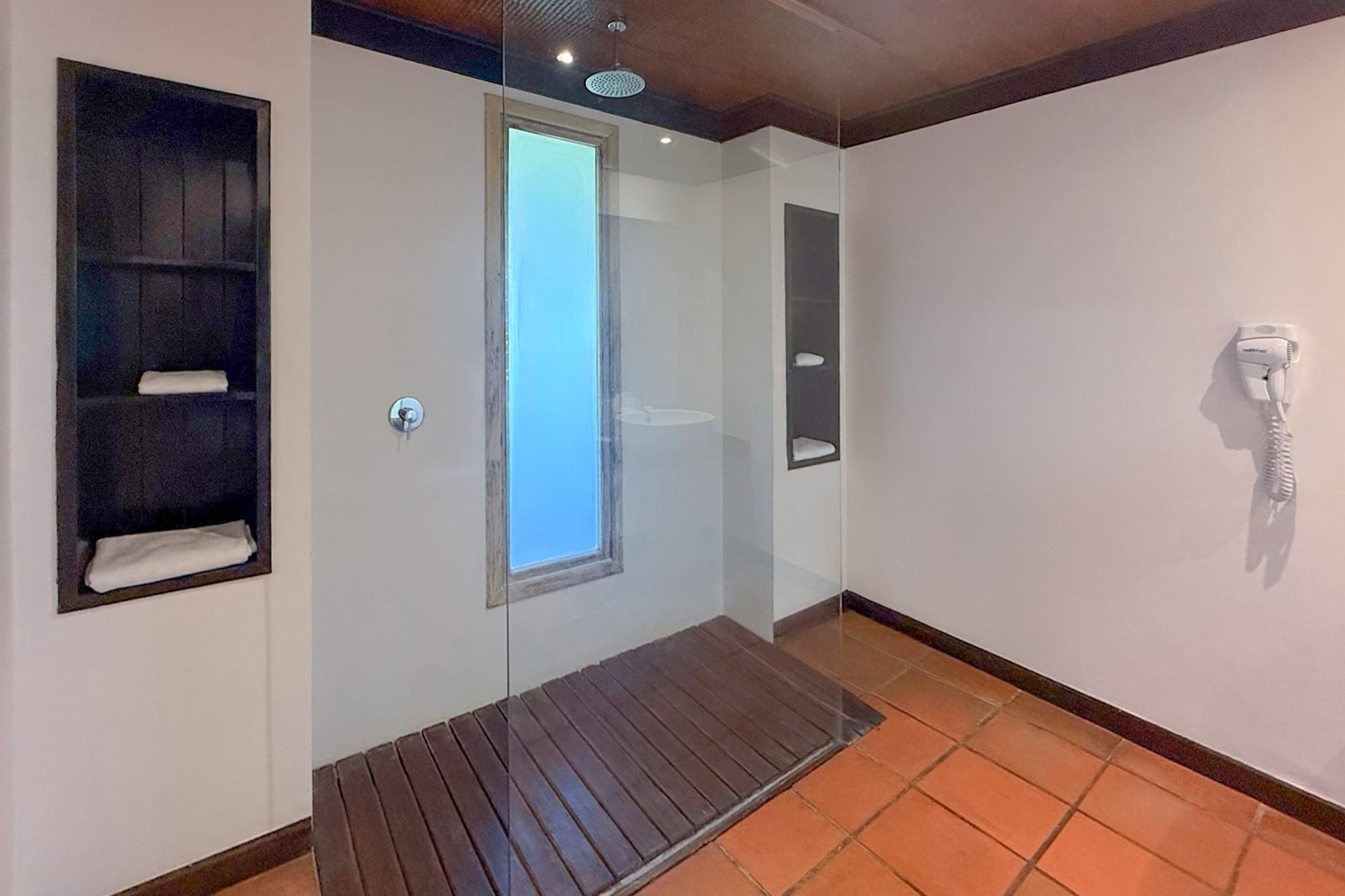 Modern bathroom with glass walk-in shower, wood floor, terracotta tiles.