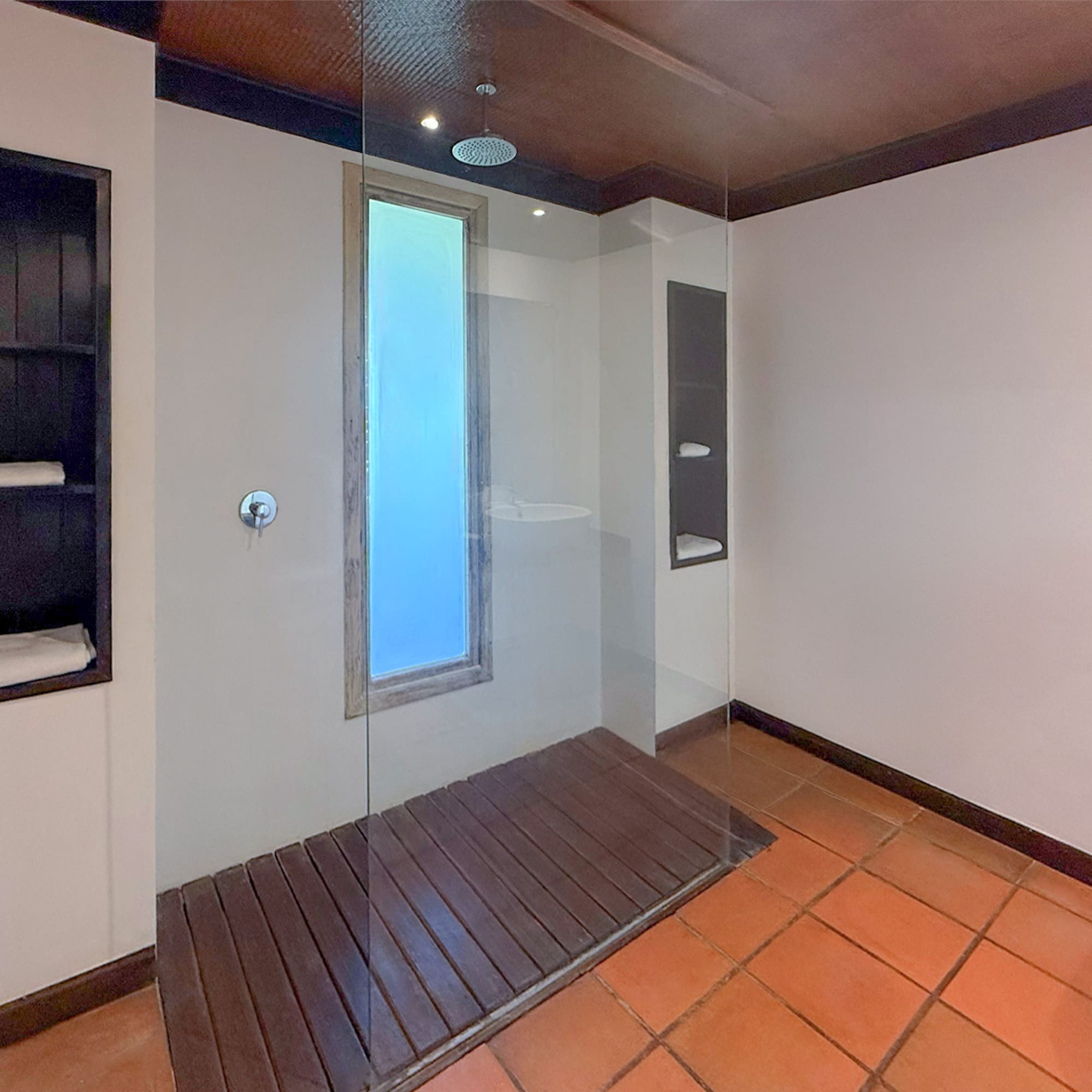 Modern bathroom with glass walk-in shower, wood floor, terracotta tiles.
