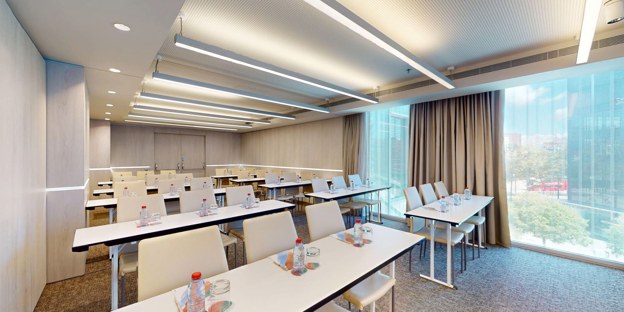 Modern meeting room with classroom setup, natural light and city view.