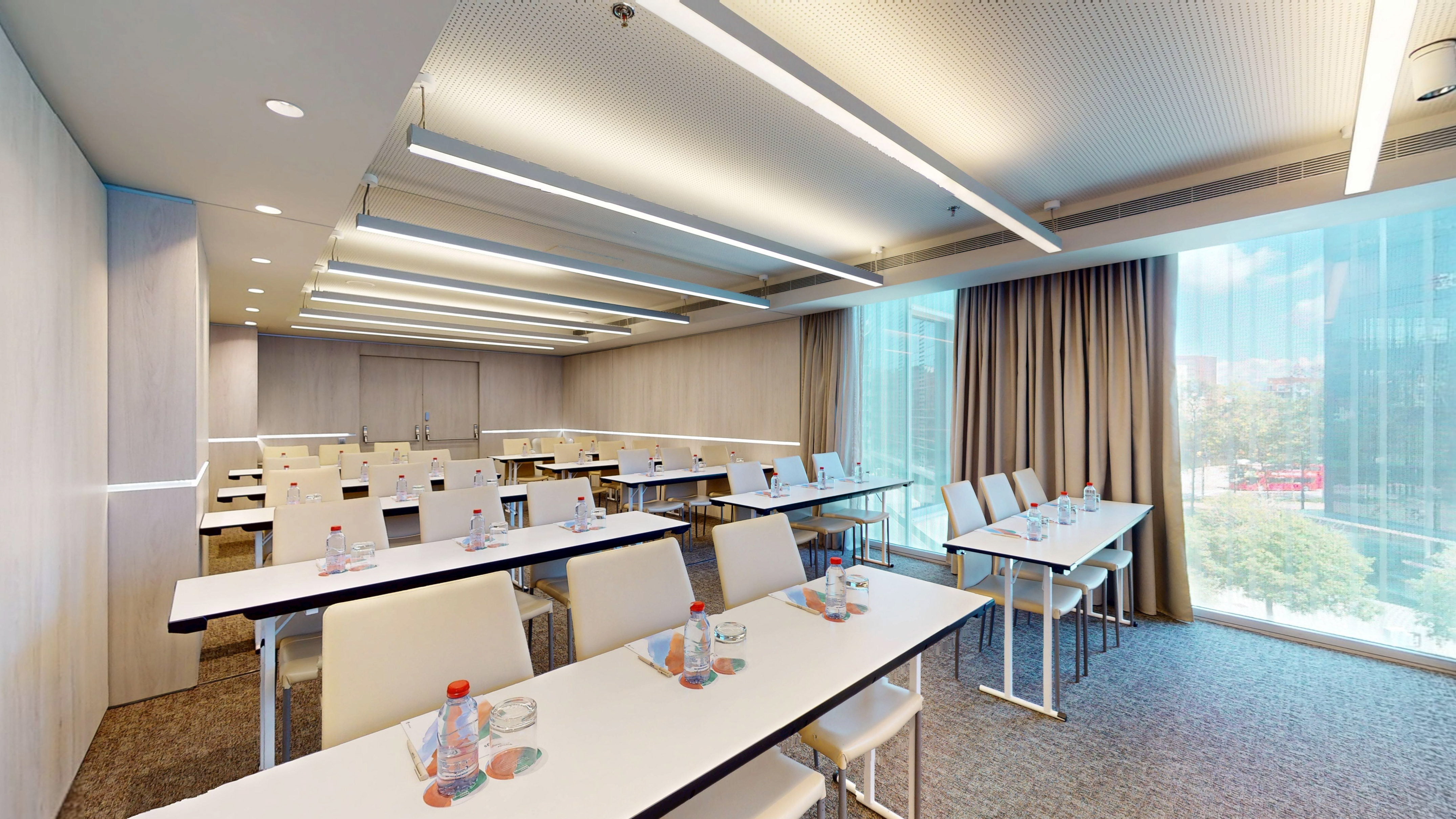 Modern meeting room with classroom setup, natural light and city view.