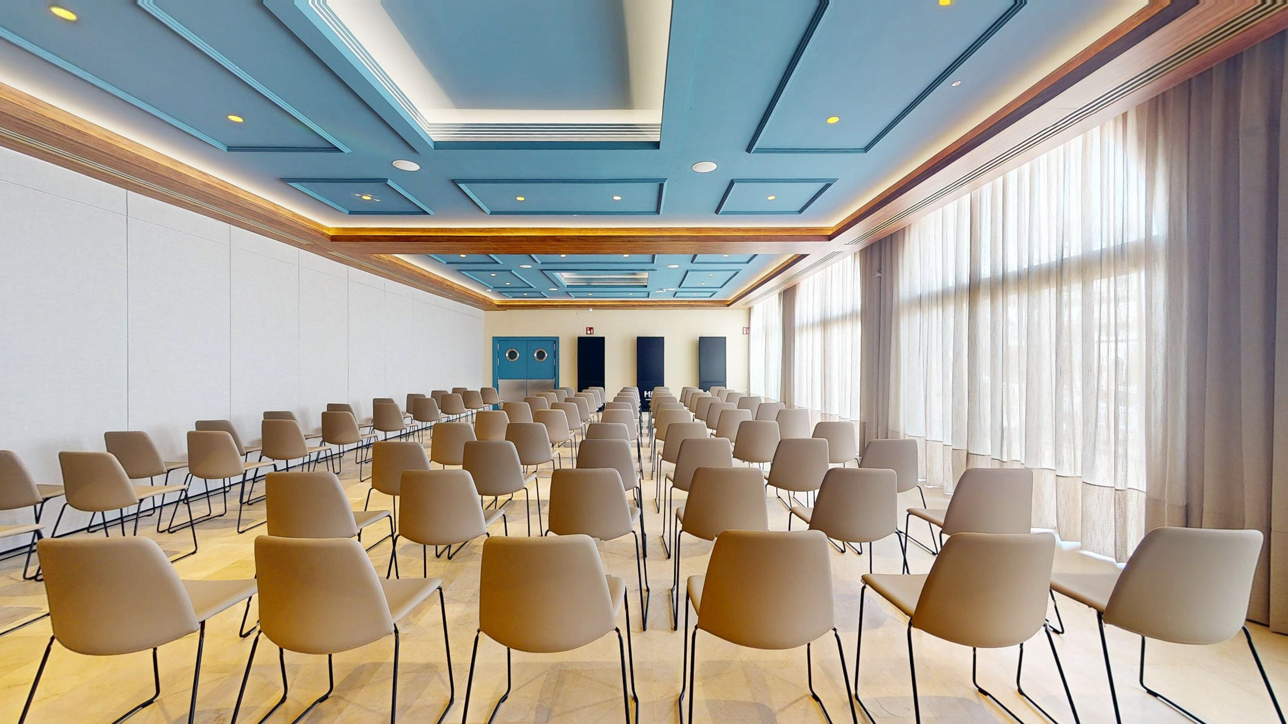 Modern conference room with tan chairs, blue ceiling, and sheer curtains.