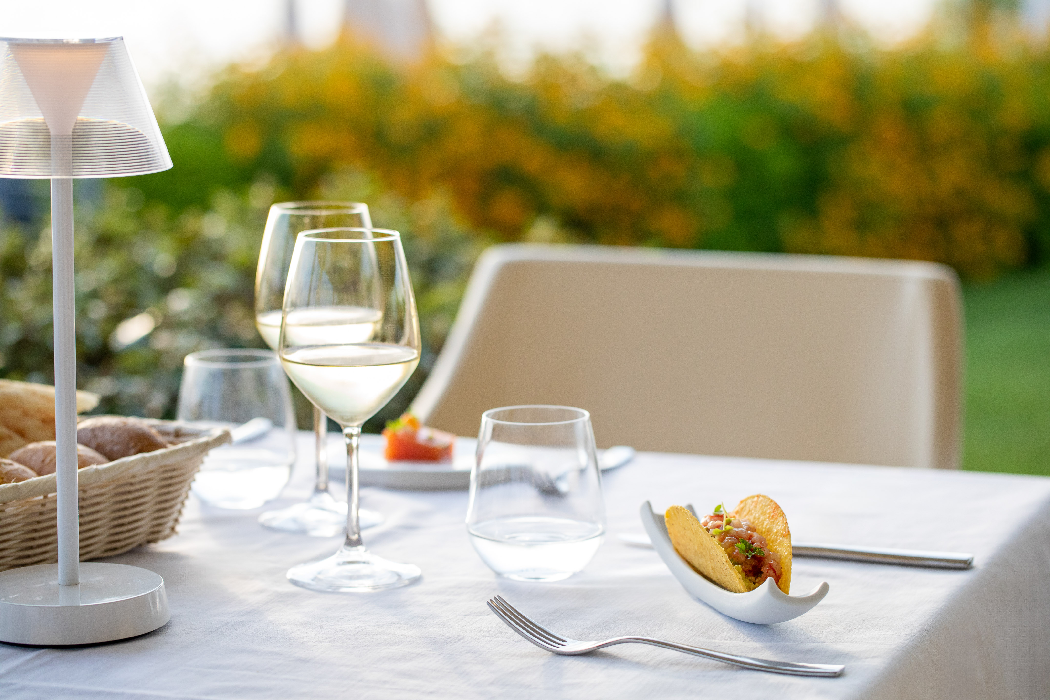 Restaurant patio table with white wine, taco appetizer, and evening lamp.