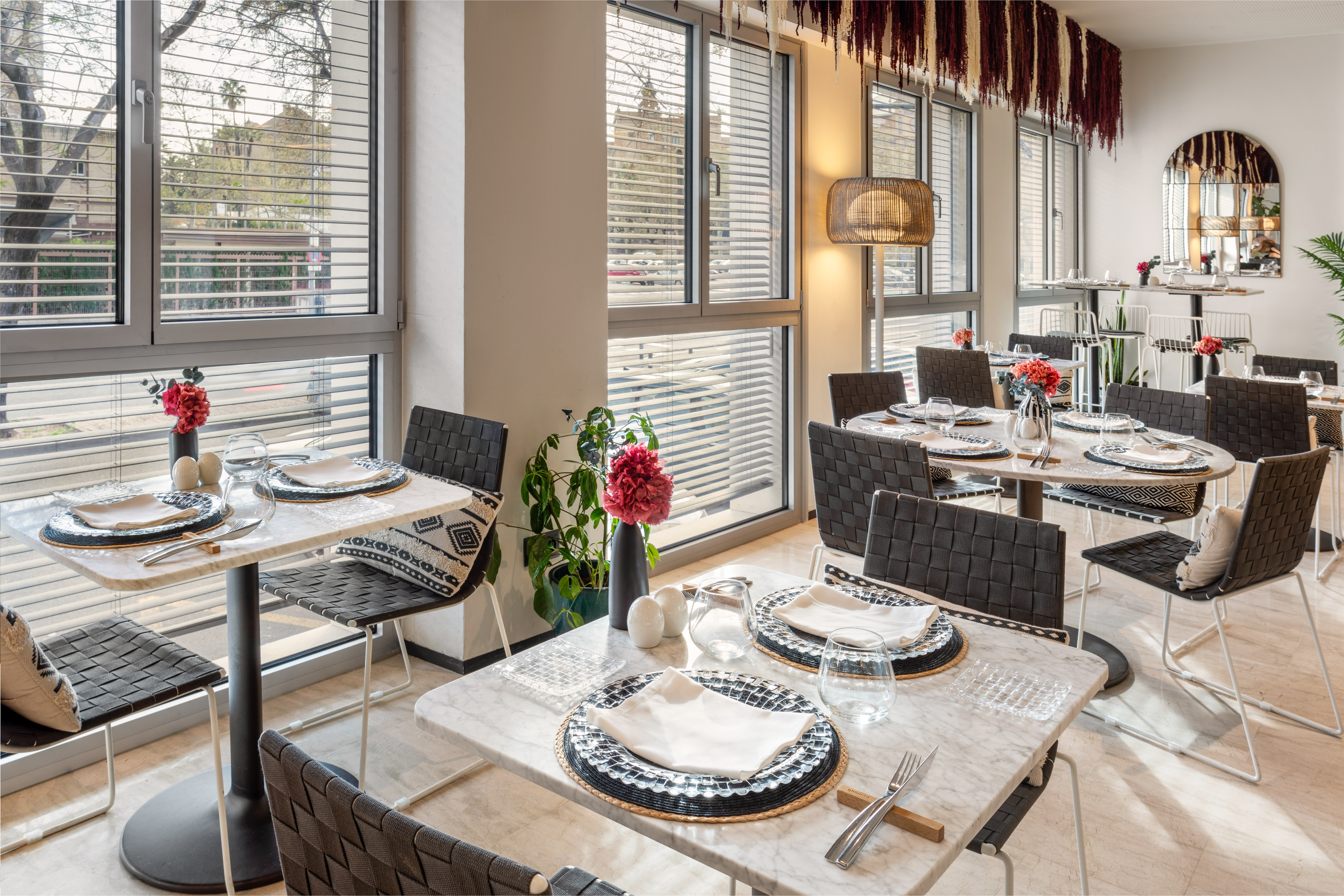 Modern restaurant with set tables, black woven chairs, and large windows.