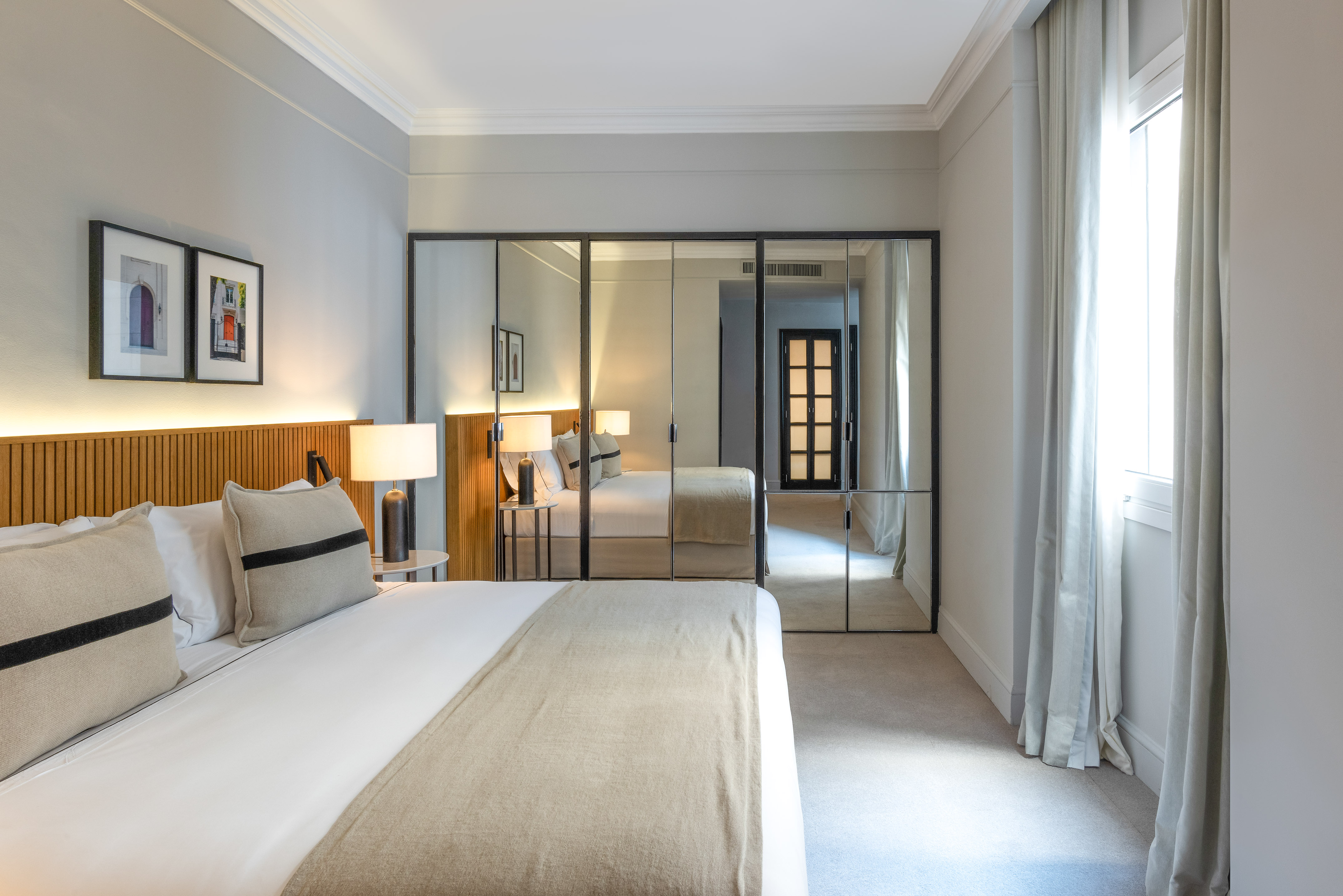 Modern hotel bedroom with large bed, slatted headboard, and mirrored wardrobe.