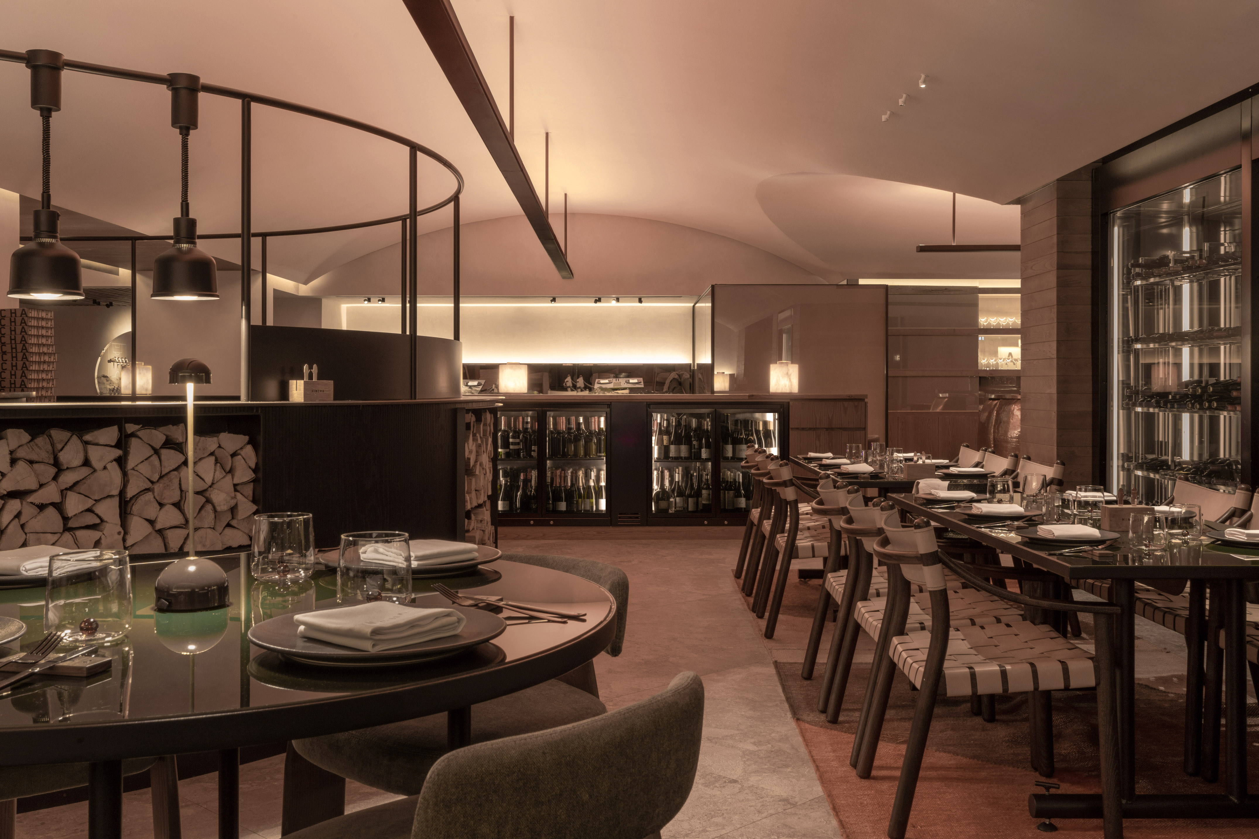 Modern restaurant interior with dining tables, warm lighting, wine storage, wood logs.