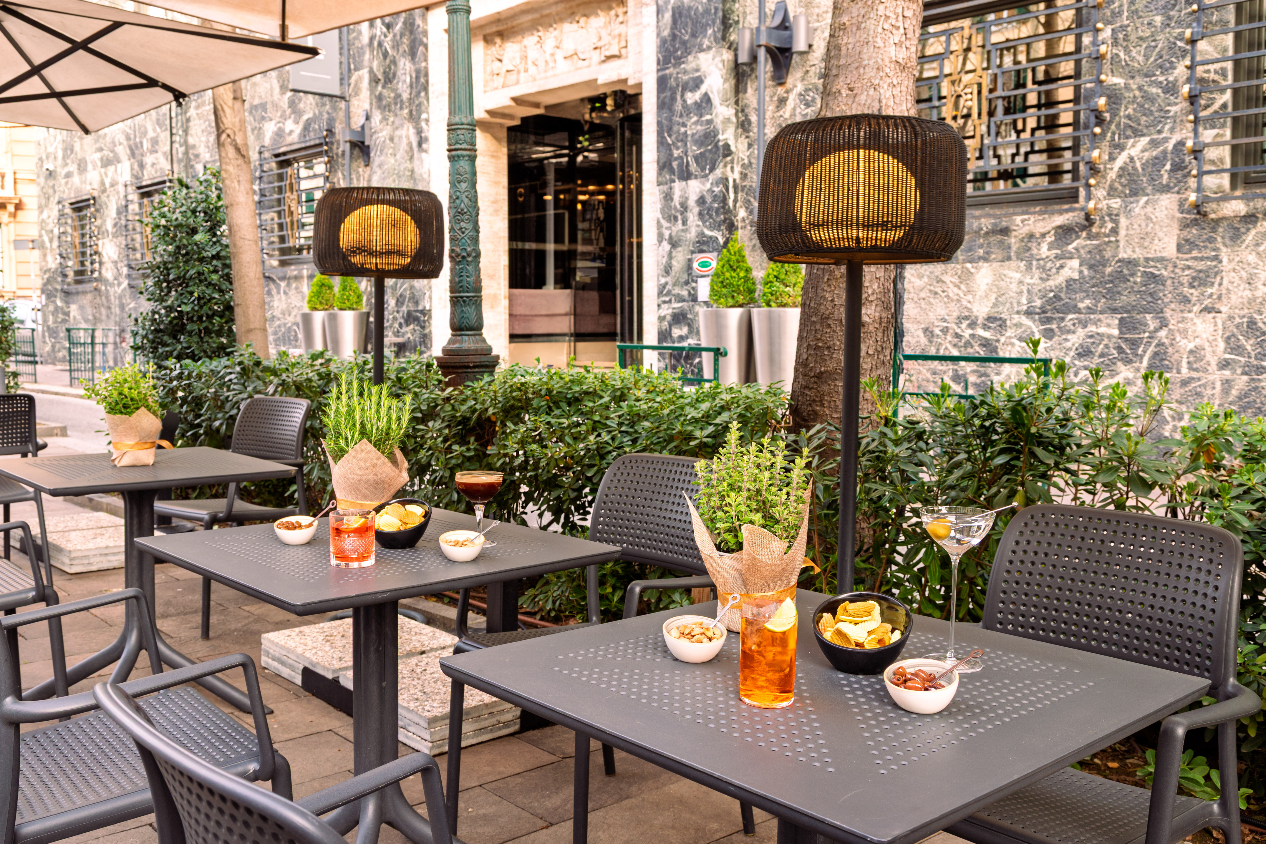 Outdoor patio cafe with cocktails, snacks, dark tables, and illuminated lamps.
